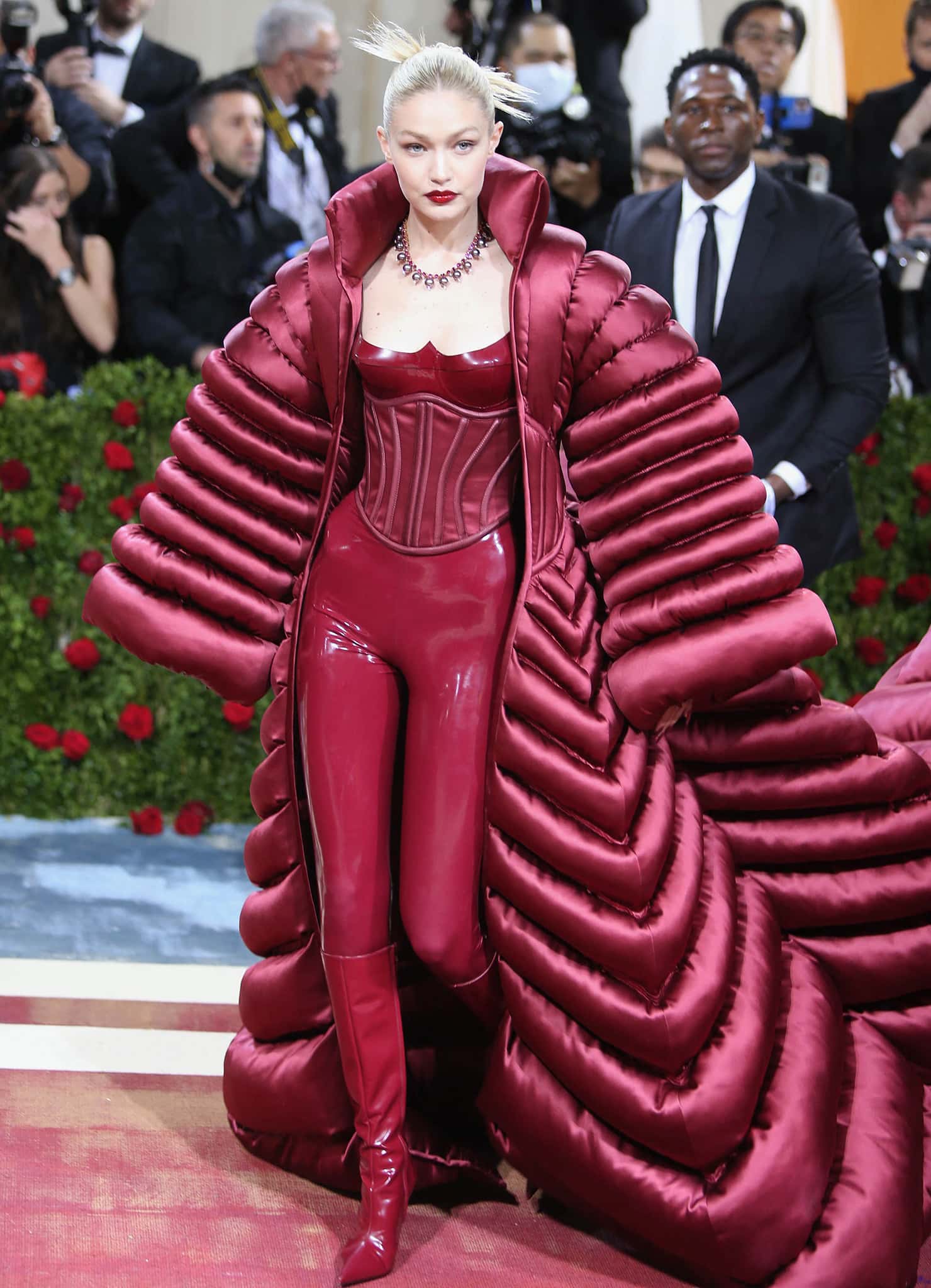 Gigi Hadid masterfully extends her burgundy latex jumpsuit into a sleek, uninterrupted silhouette with matching pointed-toe red boots