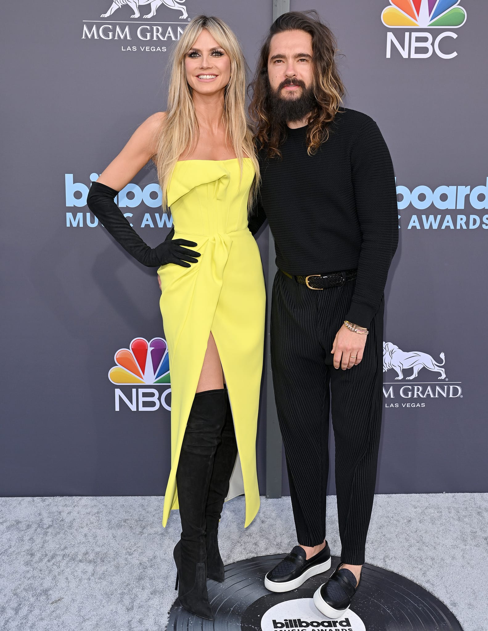Tom Kaulitz keeps the look understated in a textured black long-sleeve sweater and pleated trousers, finishing with sleek black leather loafers set on contrasting white midsoles for a subtle, modern edge alongside Heidi Klum on the red carpet