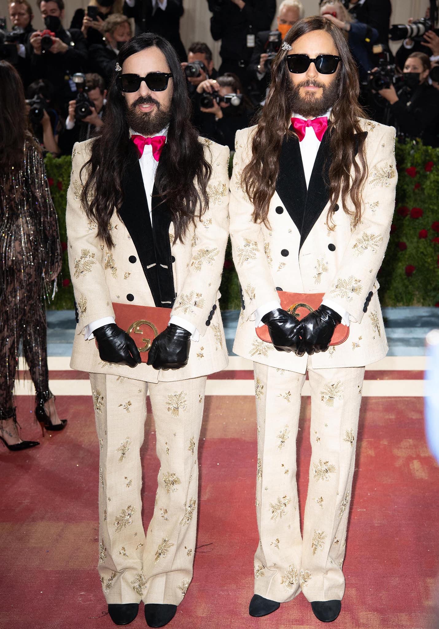Gucci creative director Alessandro Michele and Jared Leto coordinate in embroidered ivory Gucci tuxedos with black satin lapels, crimson bow ties, leather gloves, logo clutches, and black suede pointed-toe loafers