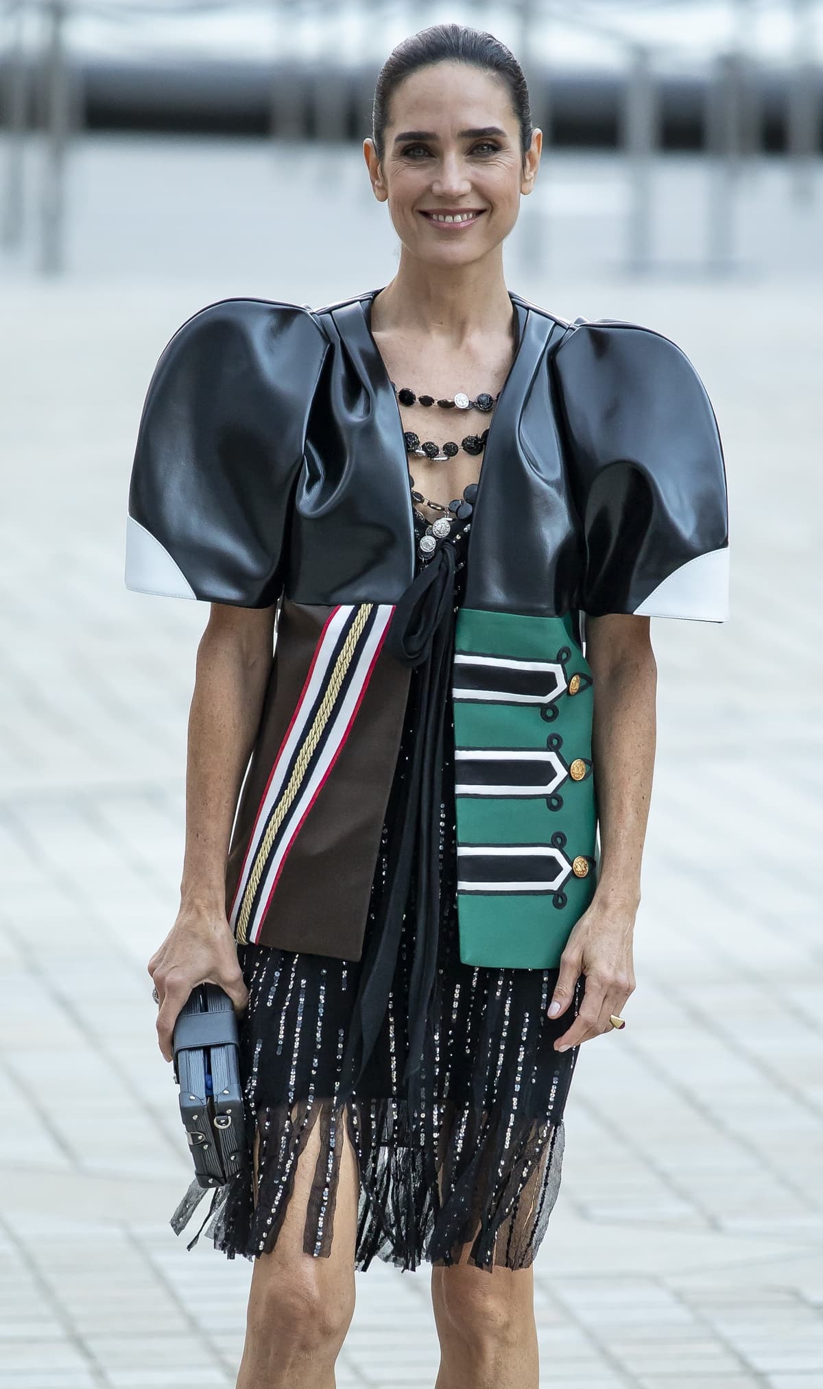 Jennifer Connelly turns heads in a striking, structured ensemble with bold shoulder details and a playful fringe skirt, paired with a chic clutch at Paris Fashion Week