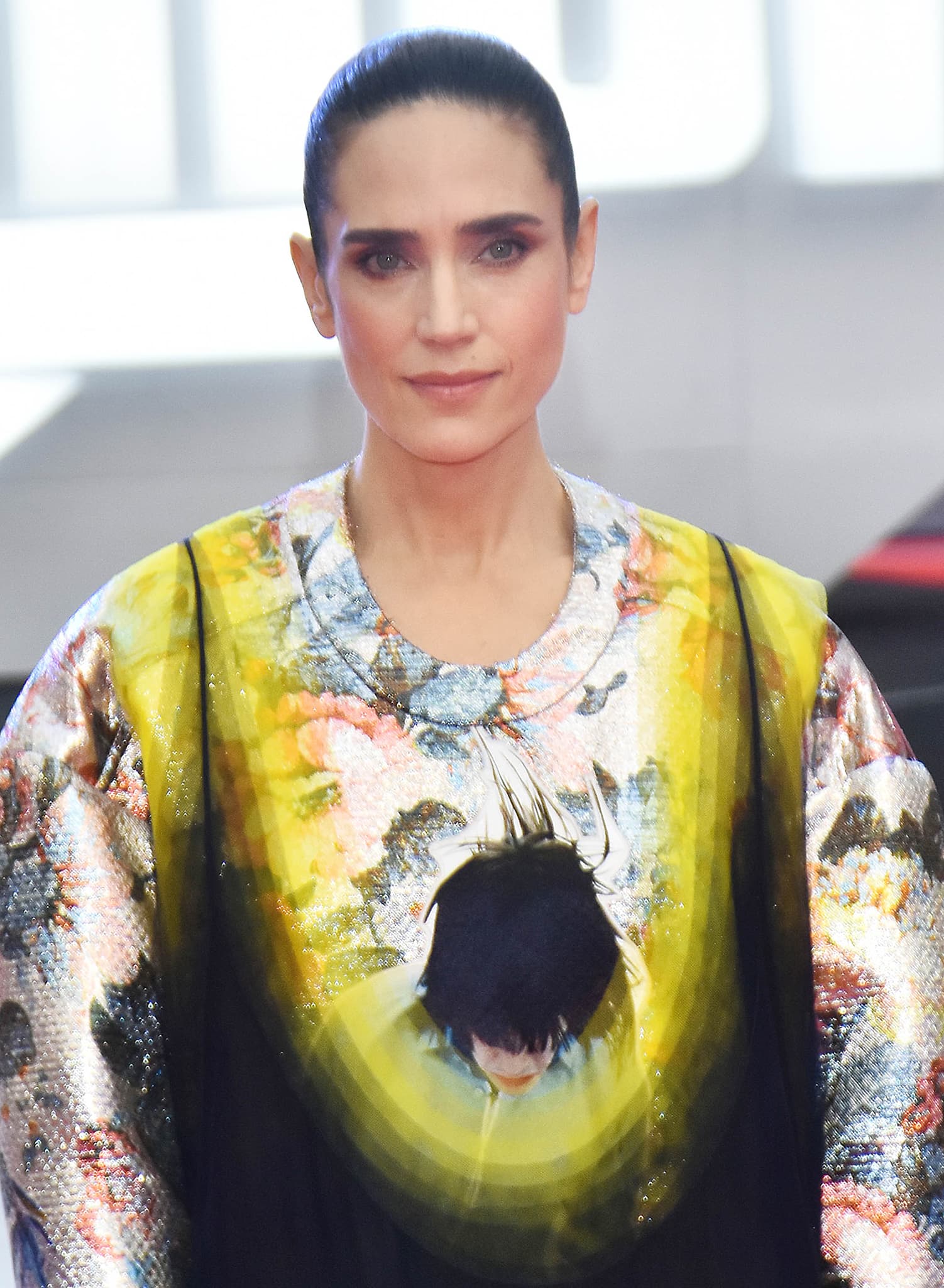 Jennifer Connelly pairs a sleek pulled-back bun with a shimmering abstract-print Louis Vuitton dress that blends metallic texture, oversized proportions, and futuristic runway drama