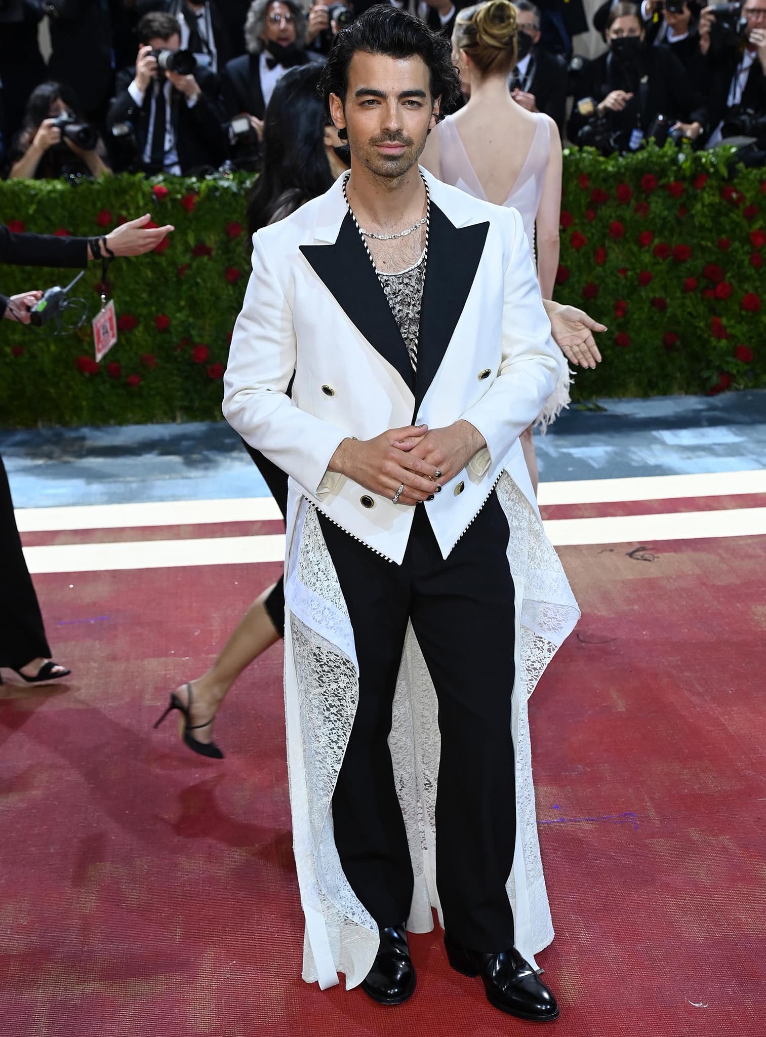 Joe Jonas makes a bold statement in a Louis Vuitton white tailcoat with contrasting black lapels and lace-panel detailing, layering a sheer lacy top beneath and finishing the look with sleek black leather dress shoes at the 2022 Met Gala