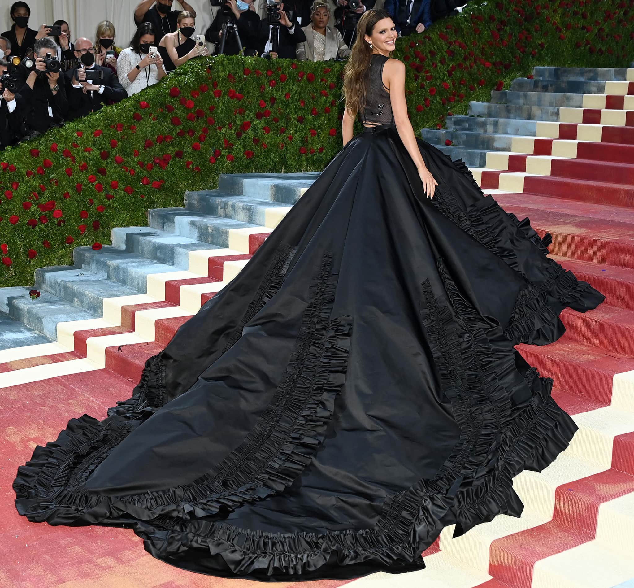 Kendall Jenner lets the sweeping scale of her custom Prada skirt take center stage, with its dramatic train designed to discreetly eclipse her minimalist heels as she moves up the Met Gala staircase