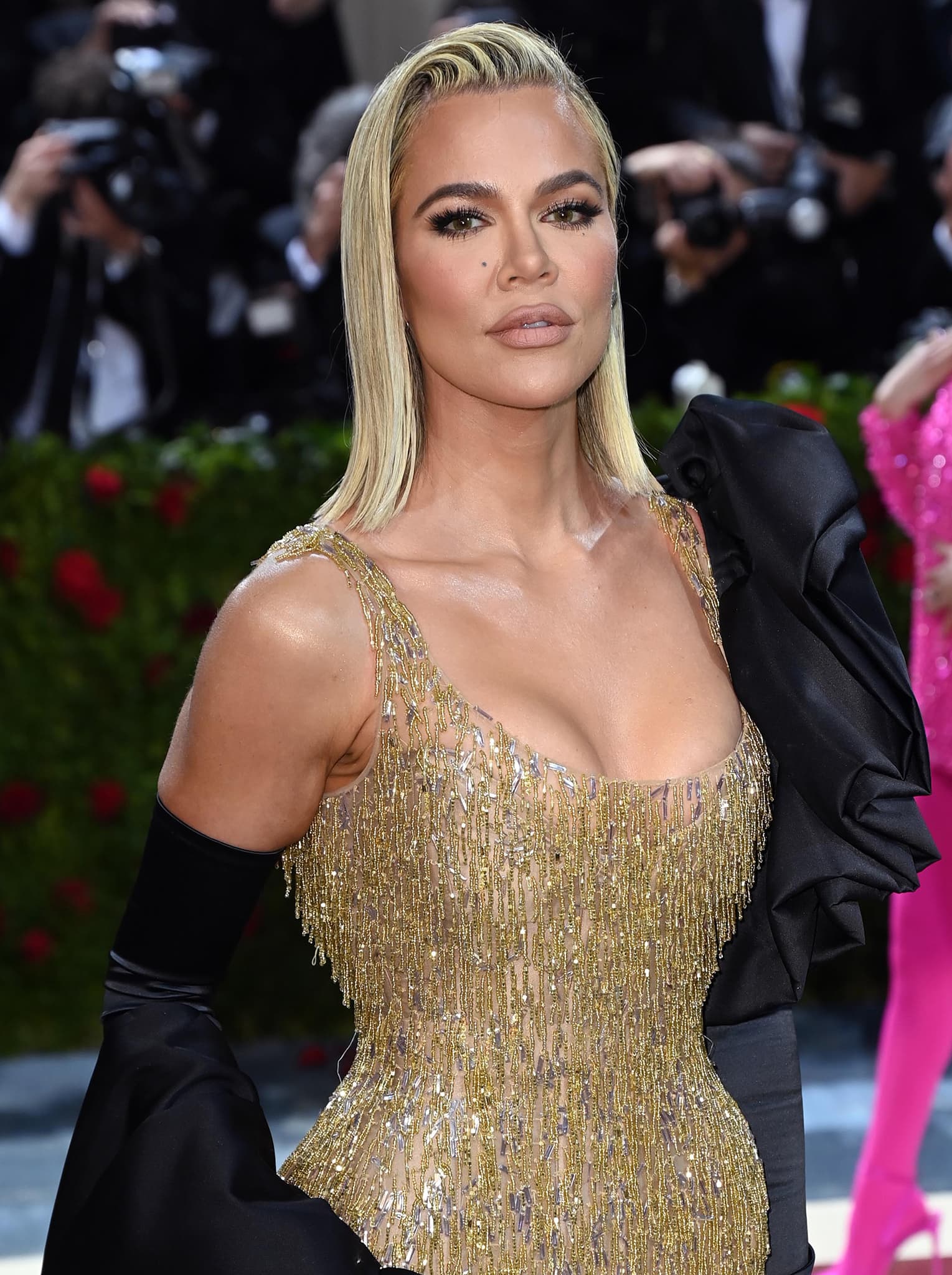 Khloé Kardashian wears a slick side-parted hairstyle with bronzed makeup, smokey eyeshadow, and matte nude lipstick