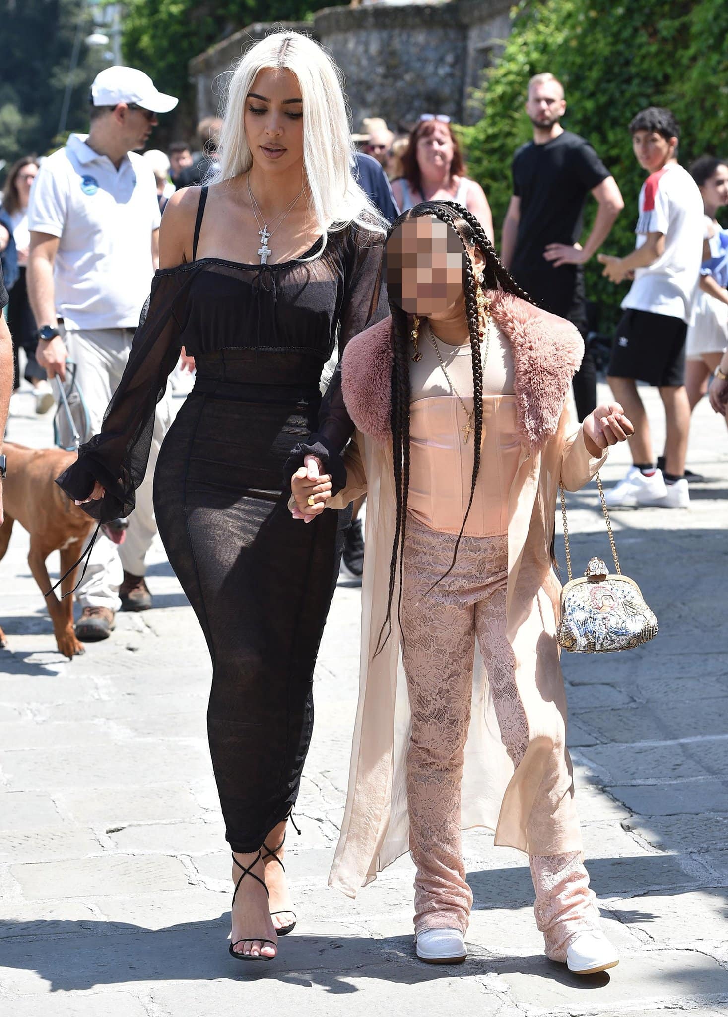 Kim Kardashian walks through Portofino in a sheer black Dolce Gabbana dress paired with delicate black crisscross-strap stiletto sandals while holding hands with daughter North West during the wedding festivities