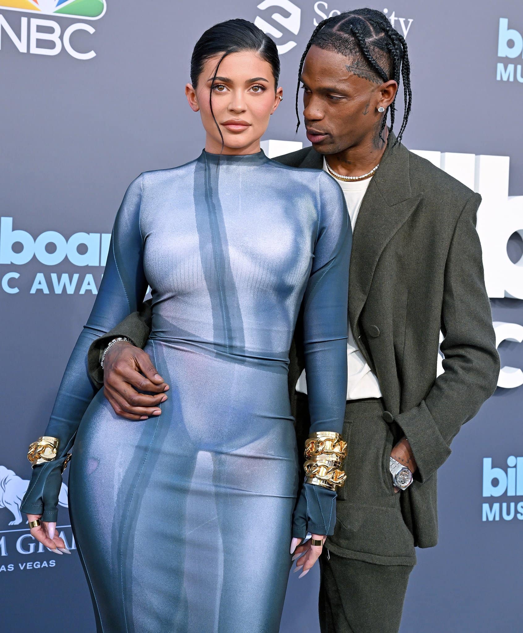 Kylie Jenner styles her dark tresses in a sleek, low, side-parted bun with a wet-look finish, complemented by a full face of matte, neutral-colored makeup featuring brown eyeshadow and a nude lip