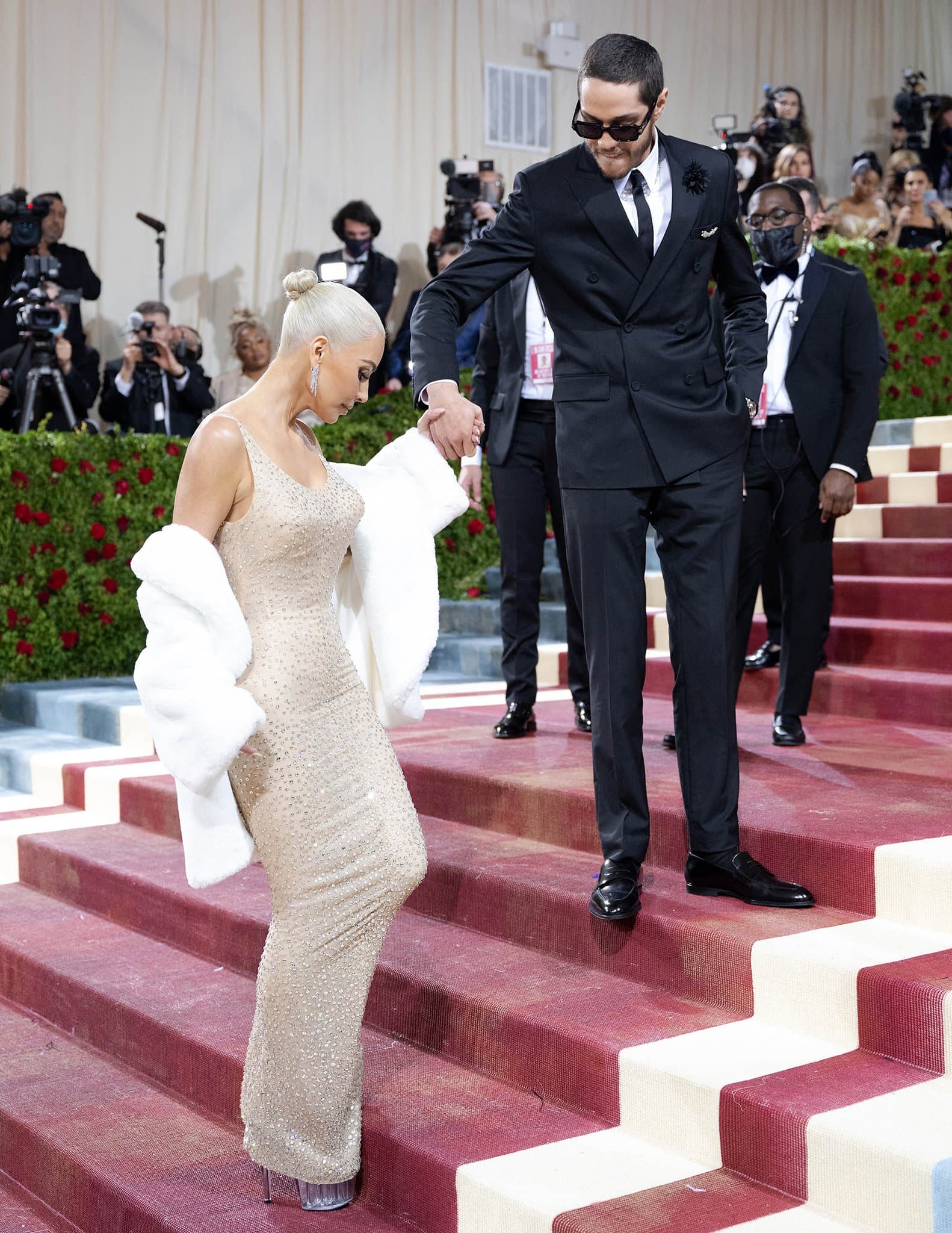 Pete Davidson steadies Kim Kardashian as she takes careful, tiny steps up the Met’s Grand Staircase in Marilyn Monroe’s gown and towering clear platform heels