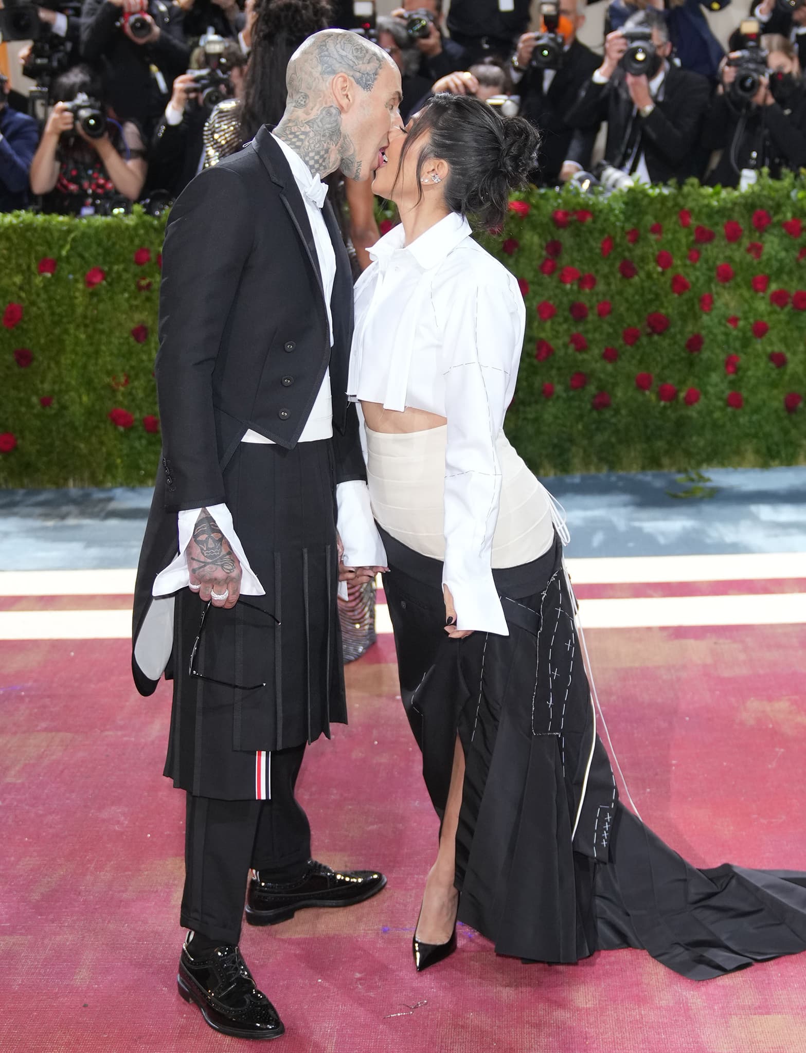 Travis Barker and Kourtney Kardashian share a playful kiss while showcasing their coordinating Thom Browne ensembles on the 2022 Met Gala red carpet
