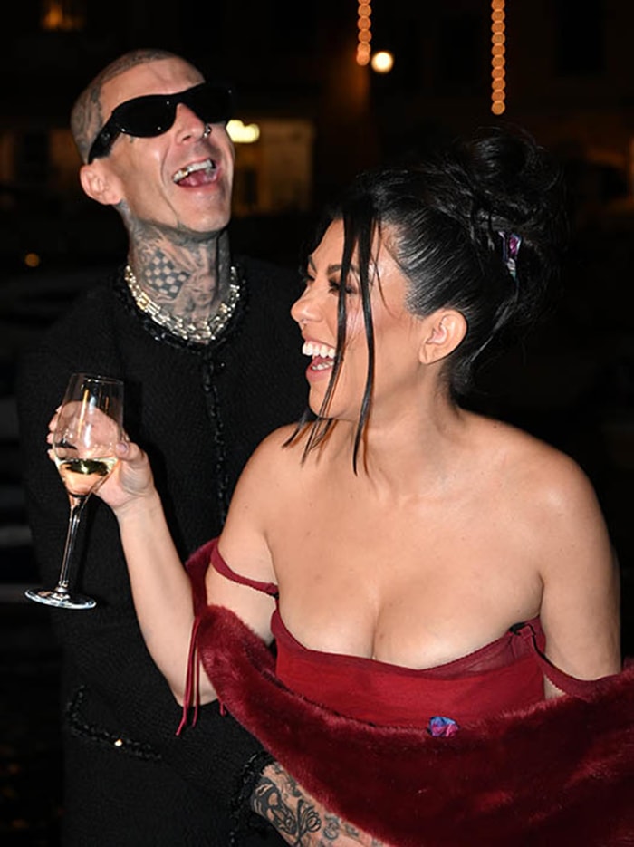 Kourtney Kardashian laughs with Travis Barker while wearing a sheer red Dolce Gabbana Spring 1998 dress layered over a bodysuit and styled with a matching fur stole during their pre-wedding dinner celebration in Portofino