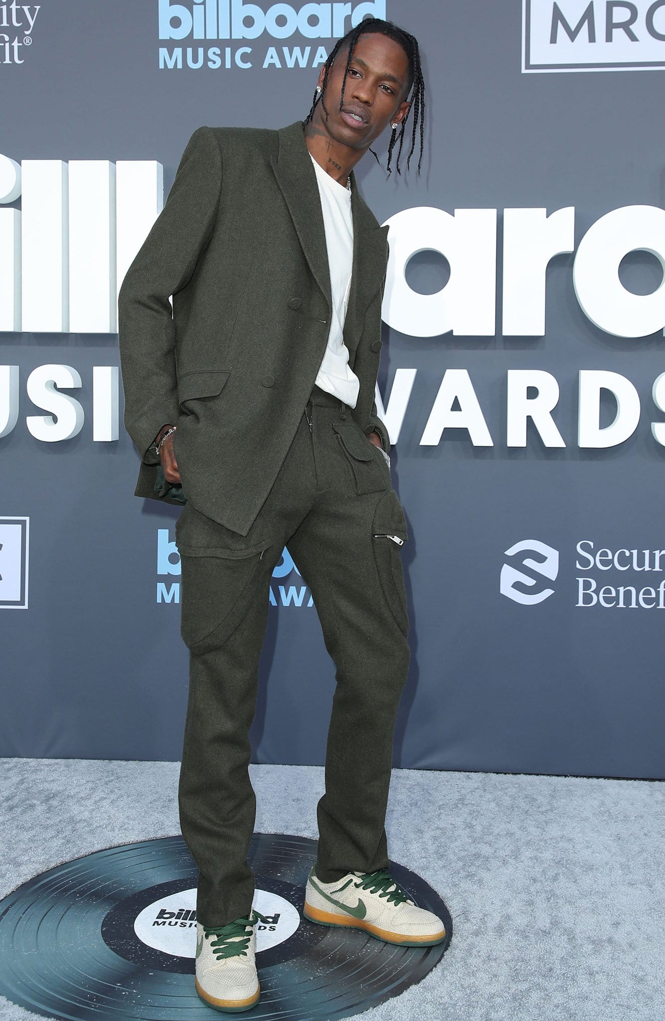 Travis Scott keeps it sharp yet laid-back at the 2022 Billboard Music Awards on May 15, 2022, pairing a structured olive green suit with a crisp white tee and his signature style twist—green and beige Nike sneakers