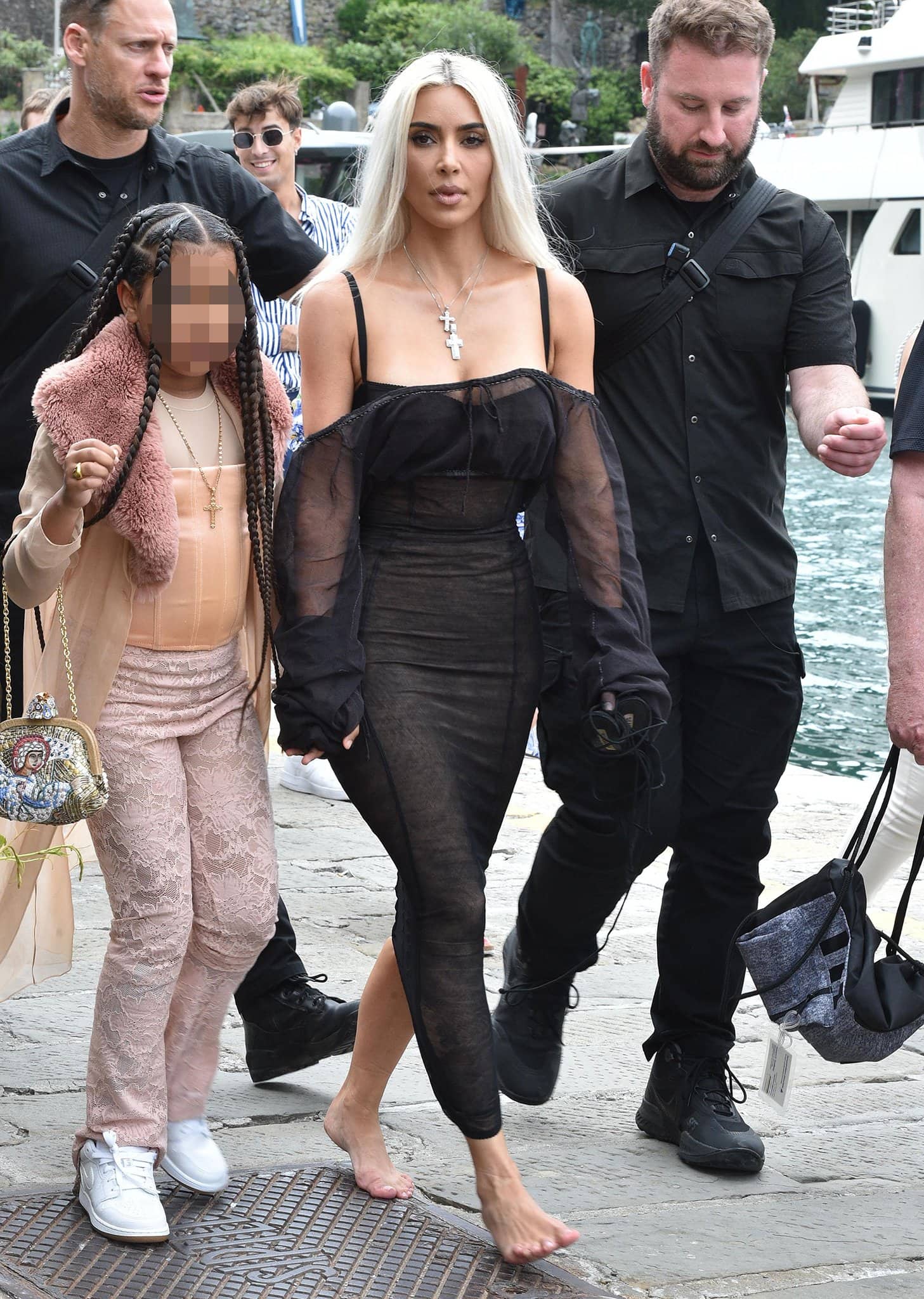 Kim Kardashian goes barefoot while walking through Portofino in a sheer black Dolce Gabbana dress, carrying her heels as she holds hands with daughter North West