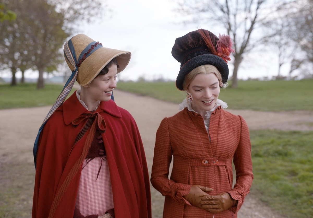 Anya Taylor-Joy brings Regency-era flair to life in EMMA., wearing a rust-toned spencer jacket with matching gloves and a dramatic feathered bonnet—perfectly capturing her character's playful elegance and social status