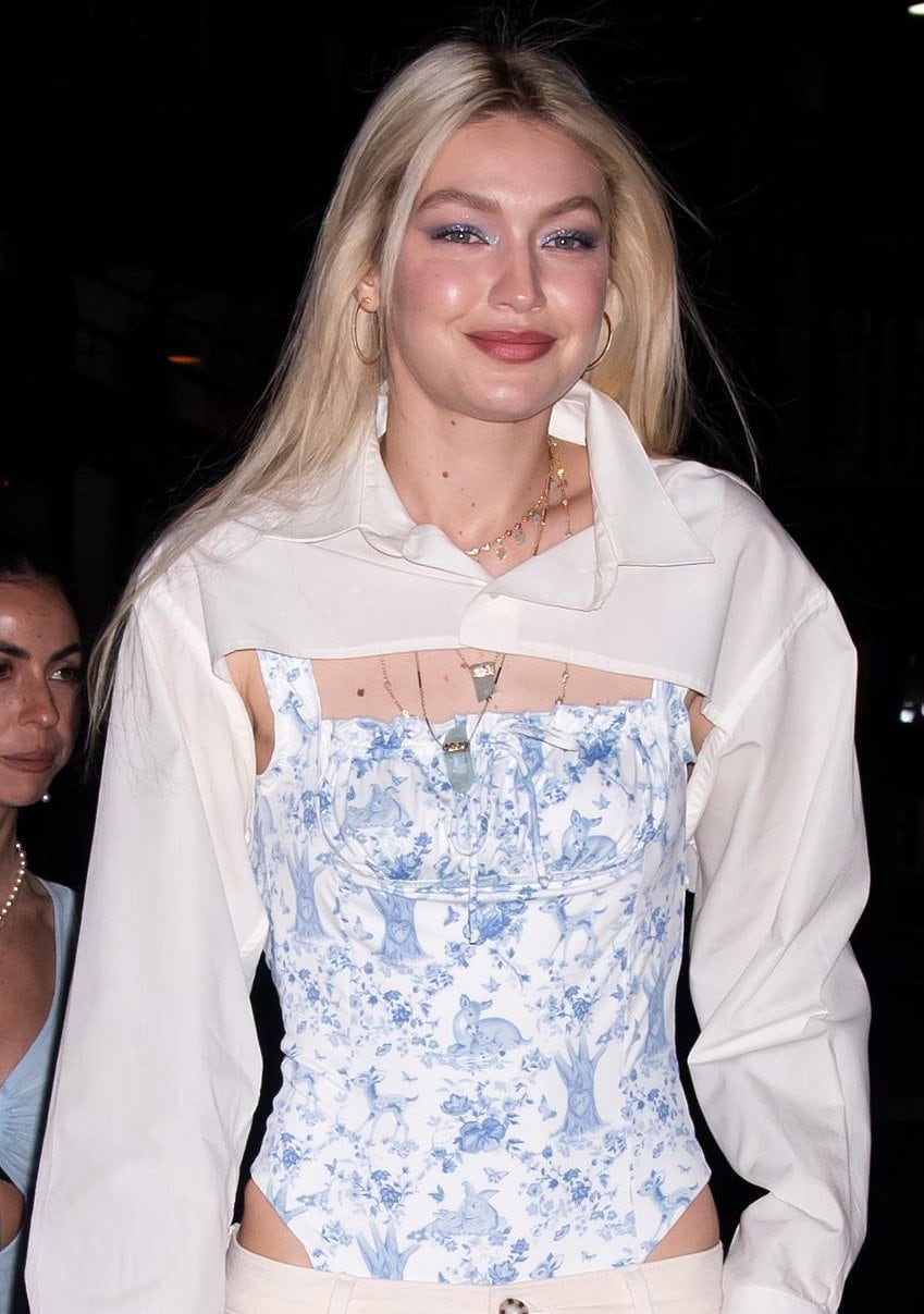 Gigi Hadid highlights the delicate blue toile detailing of her corset-style swimsuit with layered gold necklaces and soft, glowing makeup