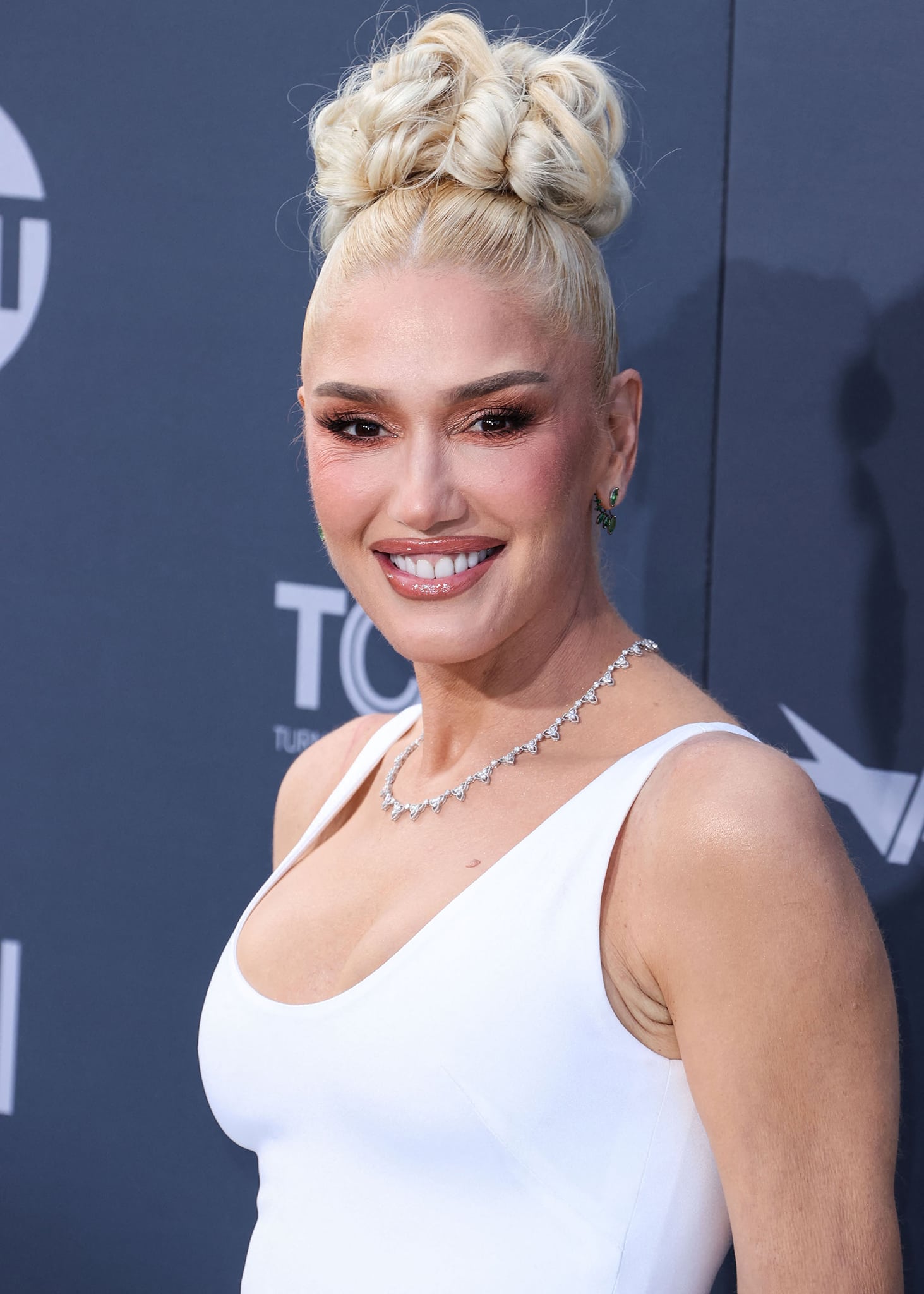 Gwen Stefani pulls her tresses up into a curled high bun and wears pink smoky eyeshadow with neutral lip gloss