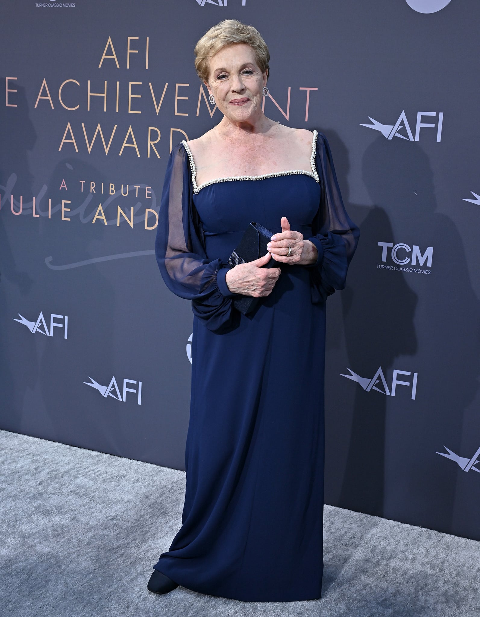 Julie Andrews radiates timeless elegance in a navy floor-length gown trimmed with delicate crystal embellishments along the neckline and sheer sleeves as she attends the 48th AFI Life Achievement Award Gala at the Dolby Theatre on June 9, 2022, celebrating a career that defined cinematic grace