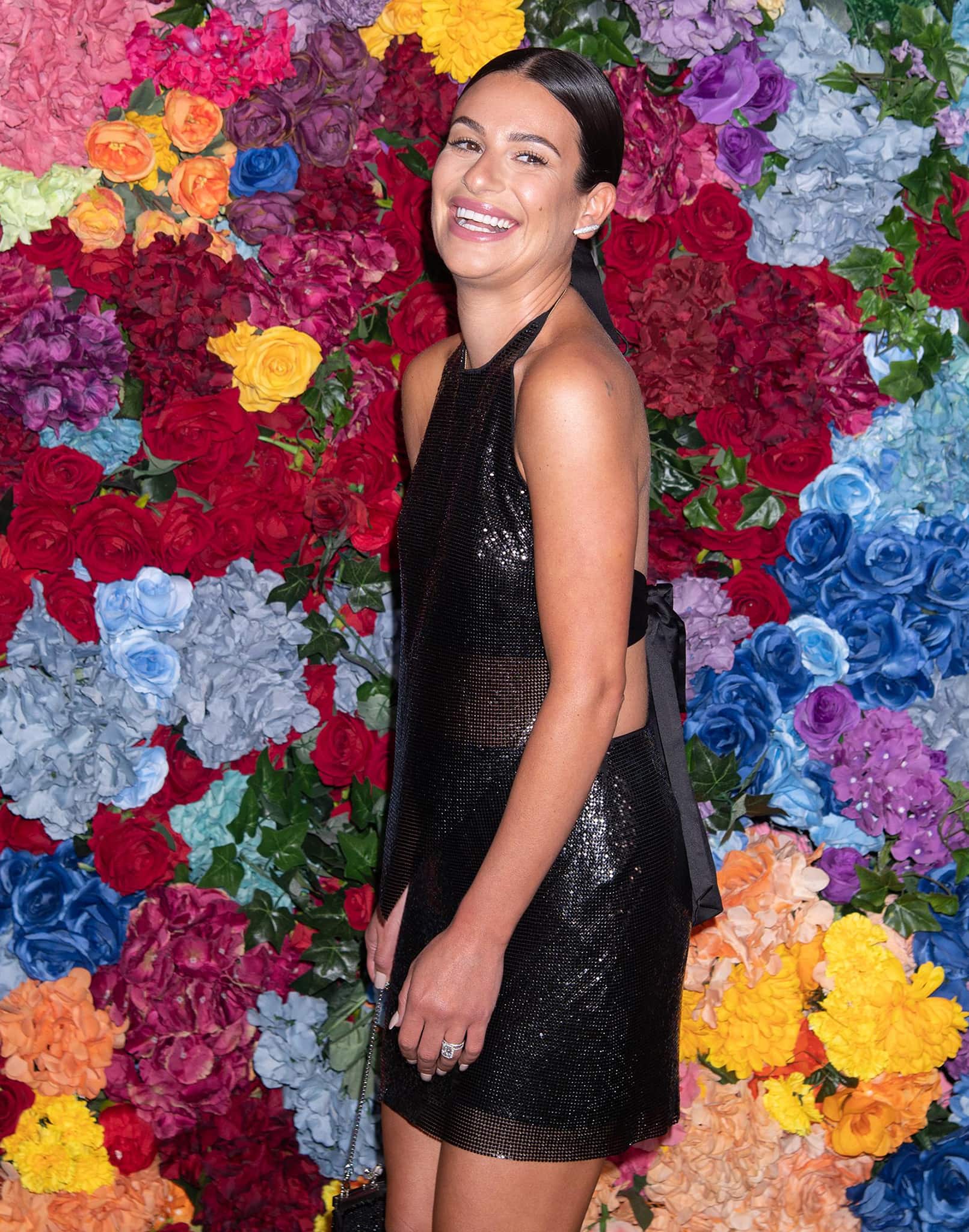 Lea Michele brings a modern edge to party dressing in Alice + Olivia’s black chainmail halter set, with the fluid metallic texture and open-back silhouette striking a balance between high-shine glamour and effortless ease against the vibrant floral backdrop