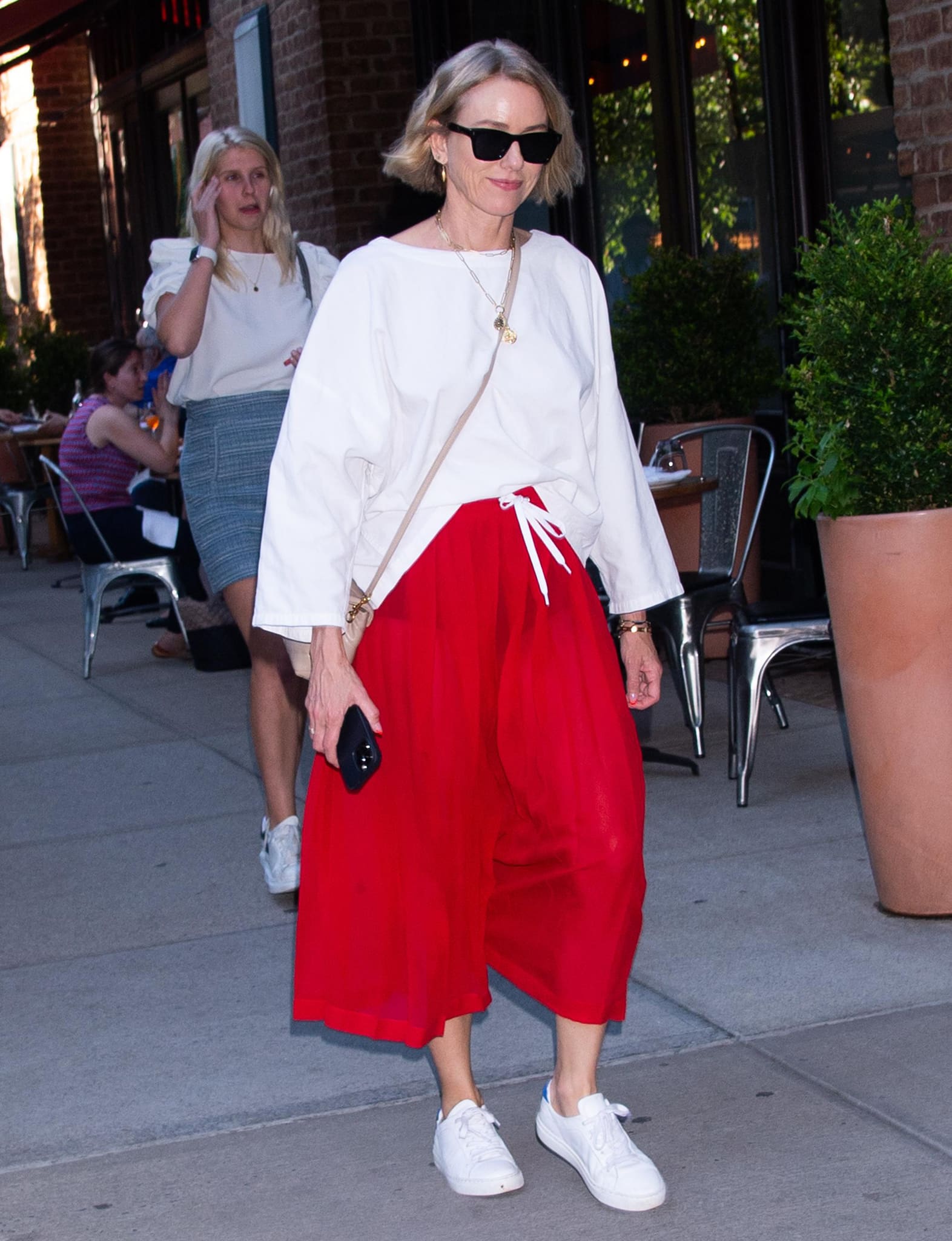 Naomi Watts swaps evening glamour for casual New York street style, pairing a relaxed white top and bright red culottes with crisp white sneakers and understated gold jewelry