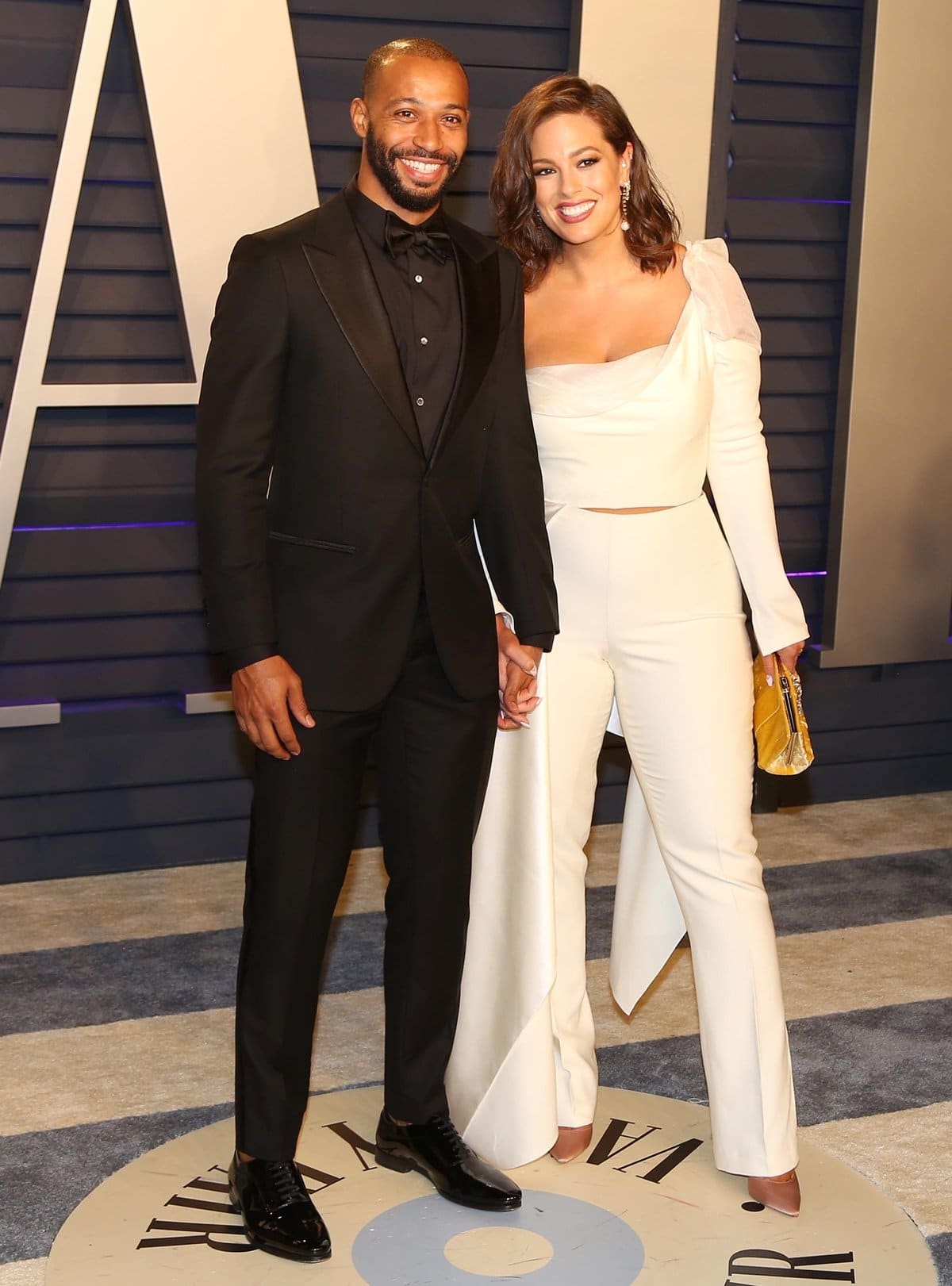 Supermodel Ashley Graham posed with husband Justin Ervin at the Vanity Fair Oscar Party in a modern white asymmetrical Prabal Gurung ensemble, styled with pointed nude heels that elongated her 5'9" frame