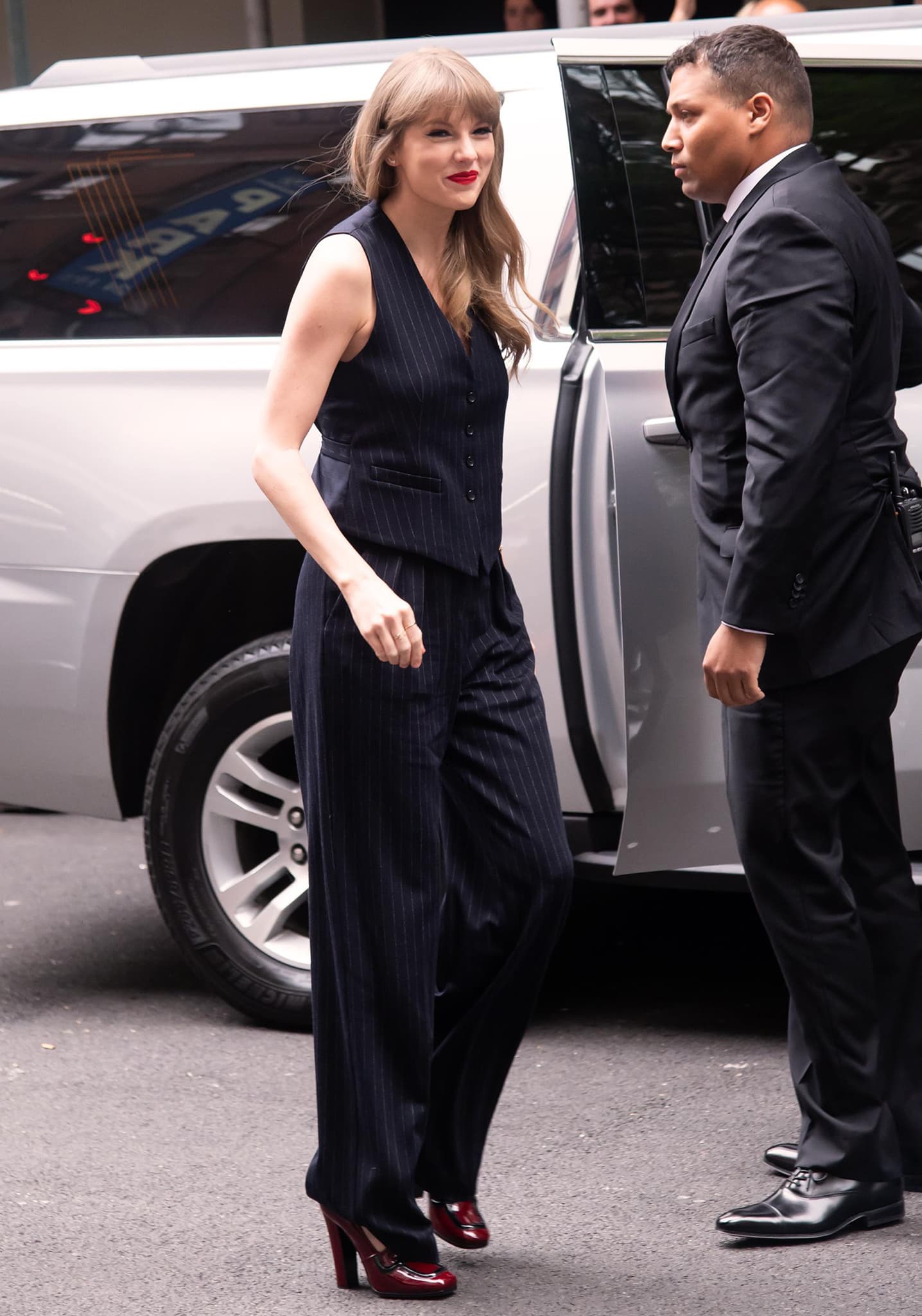 Taylor Swift steps out in a sharp navy pinstripe vest-and-trouser set, giving the tailored look a bold twist with glossy red Prada loafer pumps
