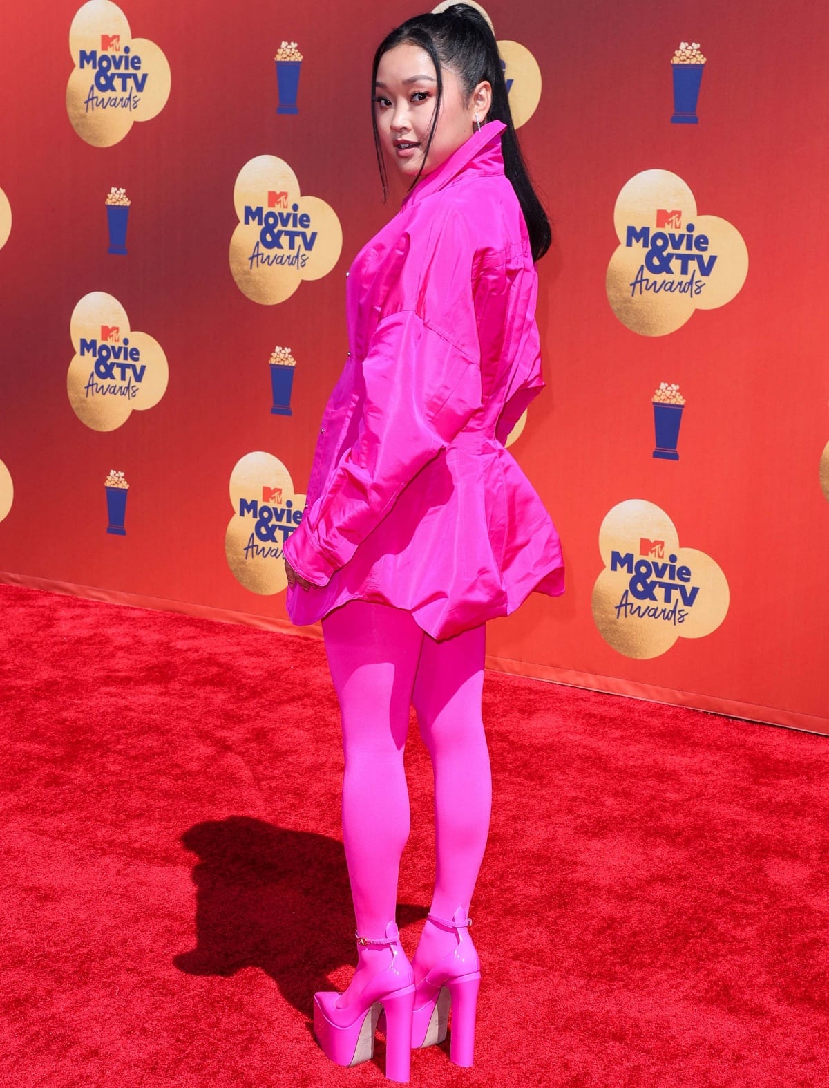 Lana Condor turns the carpet into a full Pink PP moment at the 2022 MTV Movie TV Awards, pairing her Valentino mini coat with matching tights and towering Valentino Garavani Tan-Go platform heels