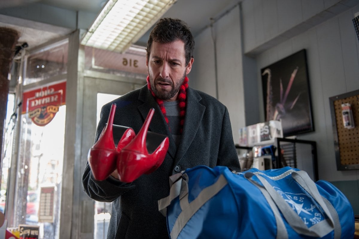 Adam Sandler, as cobbler Max Simkin, examines a striking pair of red patent leather heels that spark a magical transformation in the 2014 fantasy film The Cobbler