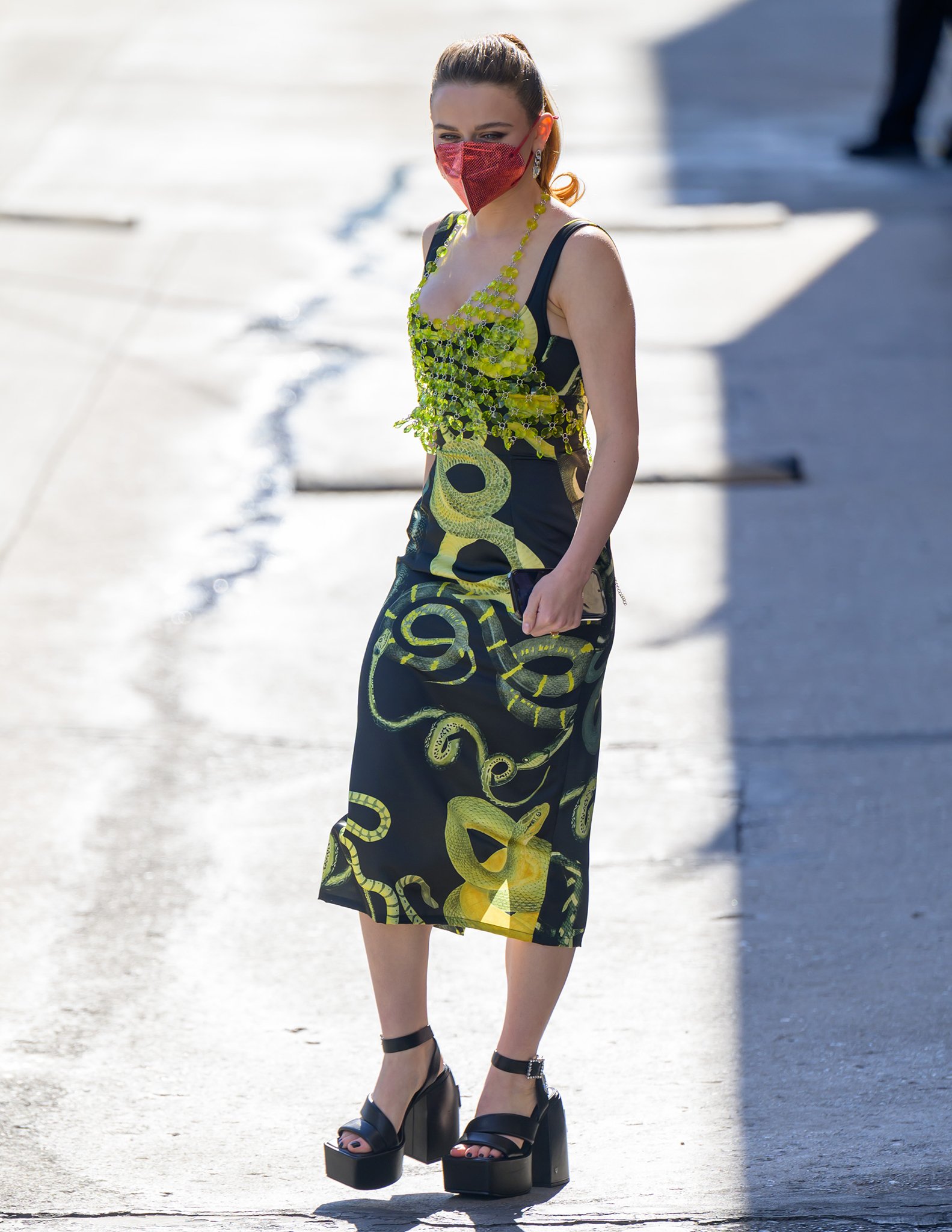 Joey King steps out in a striking Milkwhite snake-print dress topped with an Akira crystal halter and finishes the look with towering Naked Wolfe platforms and a bold red face mask