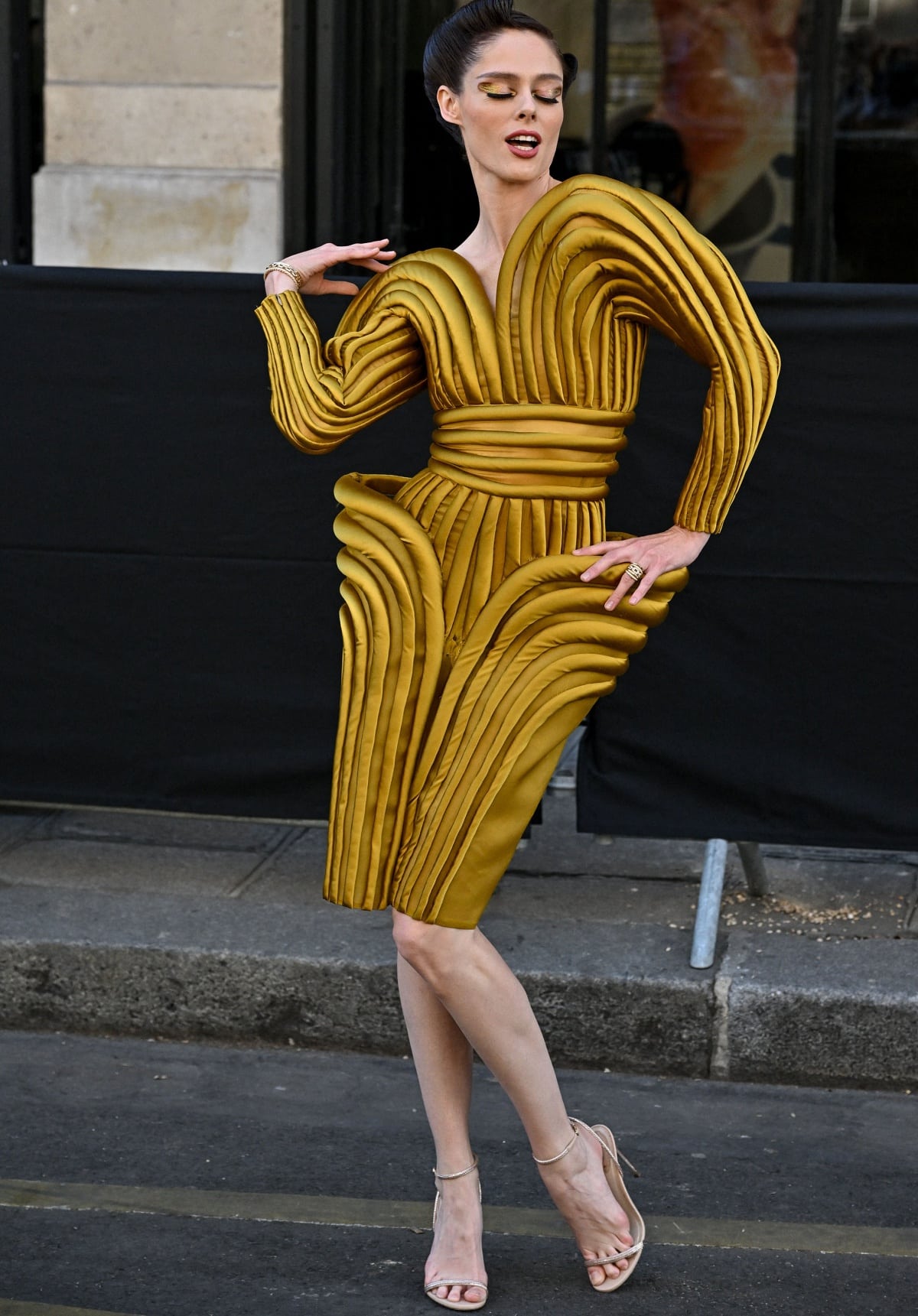 Coco Rocha showcases sculptural drama in a gold Jean Paul Gaultier archival dress paired with delicate nude ankle-strap stiletto sandals that elongate her silhouette