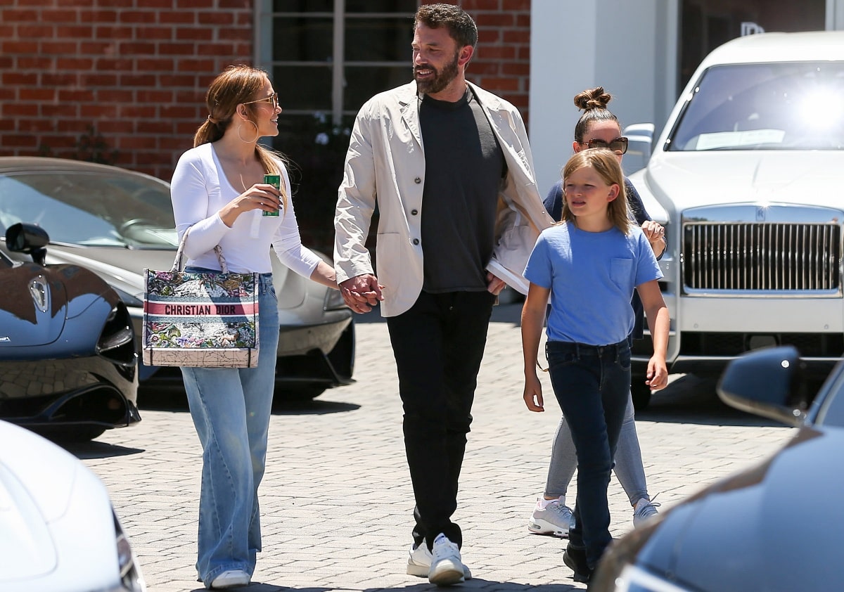Jennifer Lopez keeps her off-duty look polished in a fitted white Henley bodysuit, loose light-wash flare jeans, and white Coach sneakers while carrying a floral Dior Book Tote beside fiancé Ben Affleck and his son Samuel outside a Rolls-Royce dealership in Los Angeles on July 2, 2022
