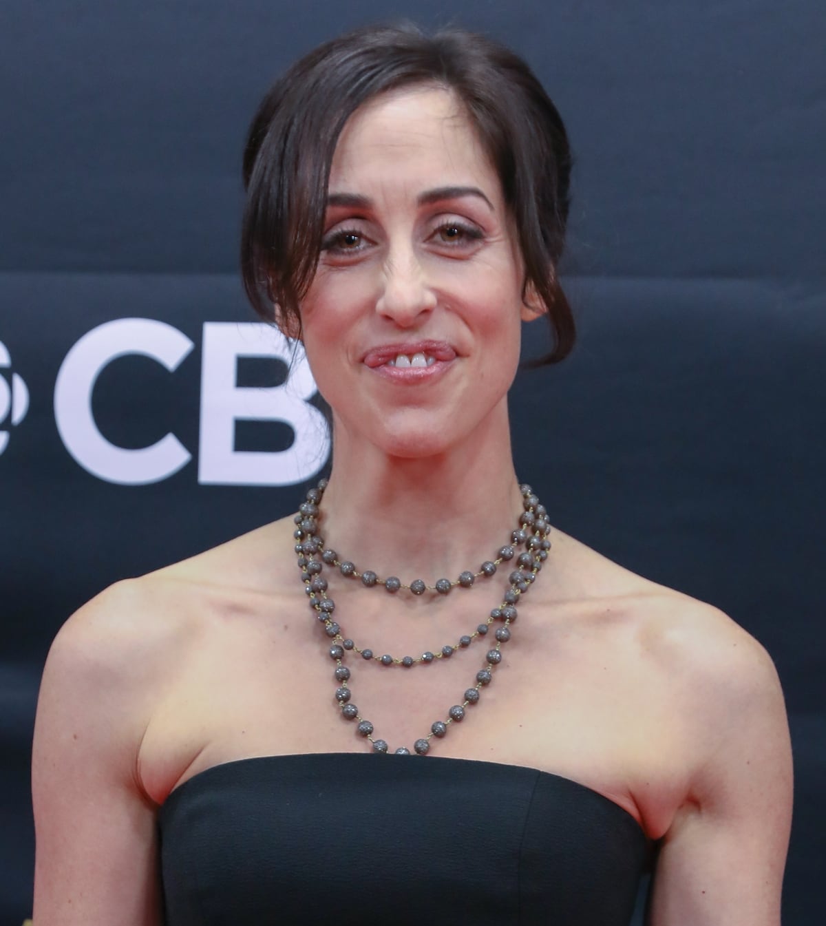 Catherine Reitman keeps her look sleek and refined in a strapless black neckline, elevated by layered beaded necklaces that draw attention to her signature, expressive smile