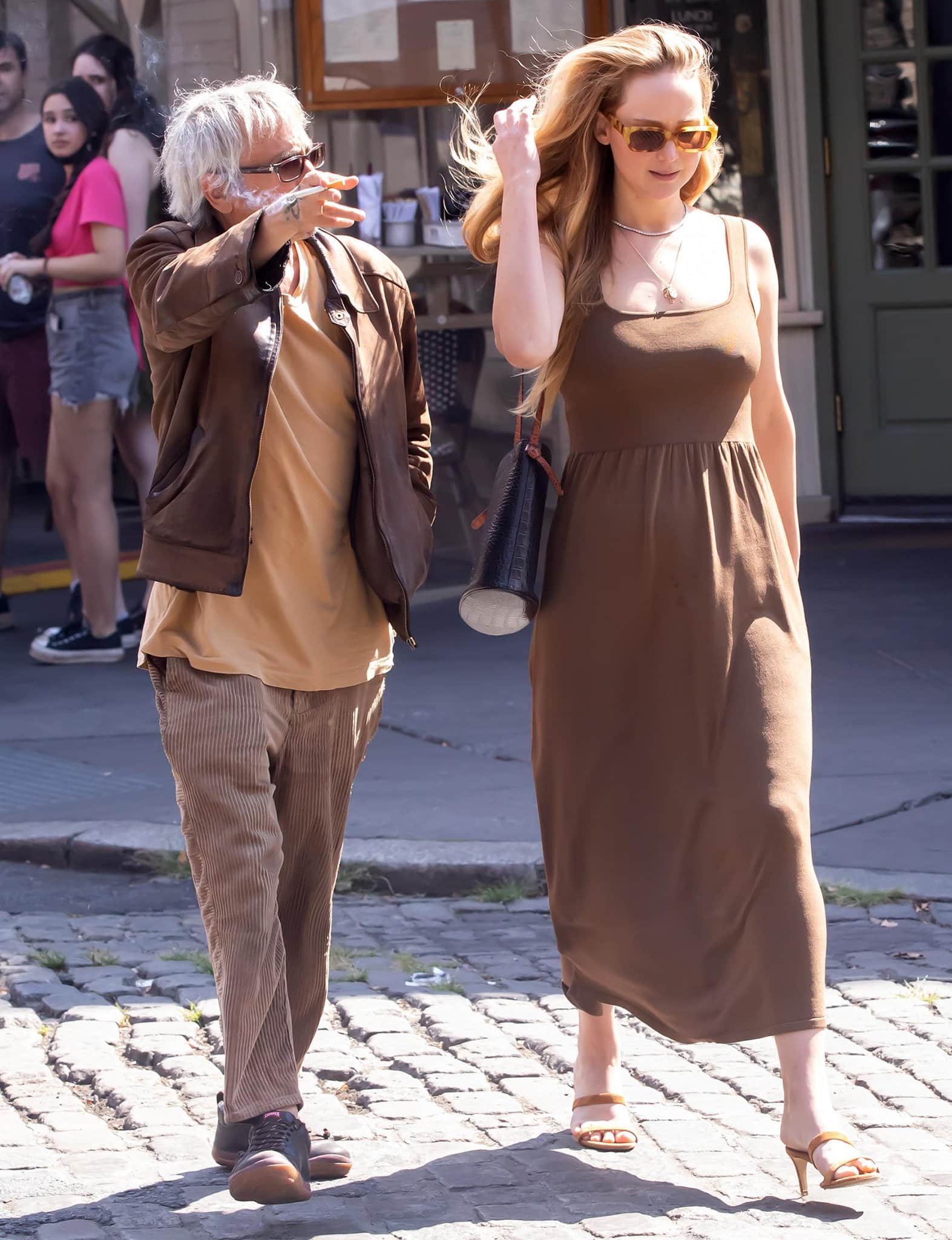 Jennifer Lawrence steps out in a brown Matteau jersey dress and open-toe heeled sandals, coordinating effortlessly with Leos Carax, who sports corduroy pants, a leather jacket, and black sneakers