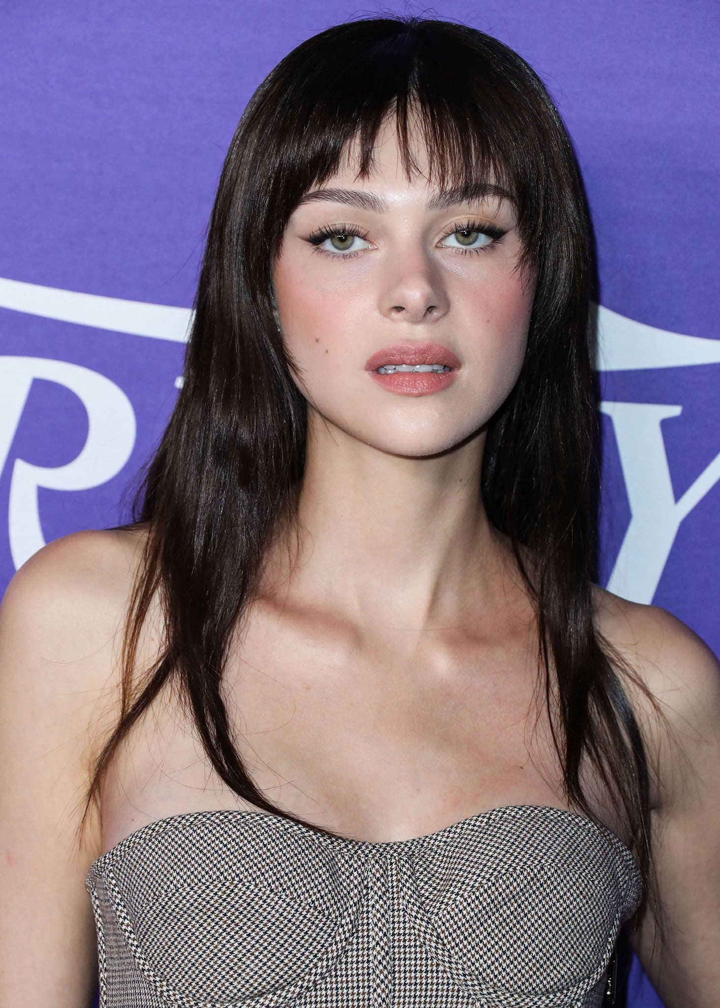 Nicola Peltz dyes her blonde hair brunette and wears cat eye-makeup with pink blush and lipstick