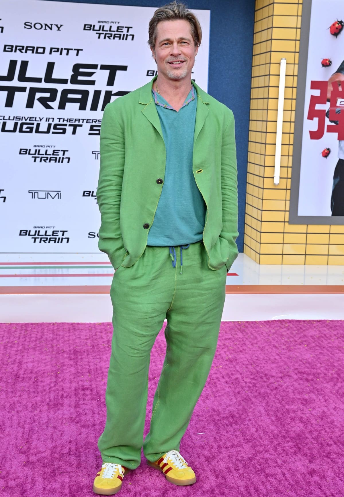 Brad Pitt exudes laid-back sophistication in a custom Haans Nicholas Mott green linen suit, paired with a teal shirt and Gucci × Adidas yellow velvet sneakers featuring signature red stripes — a playful, fashion-forward twist on classic red-carpet tailoring