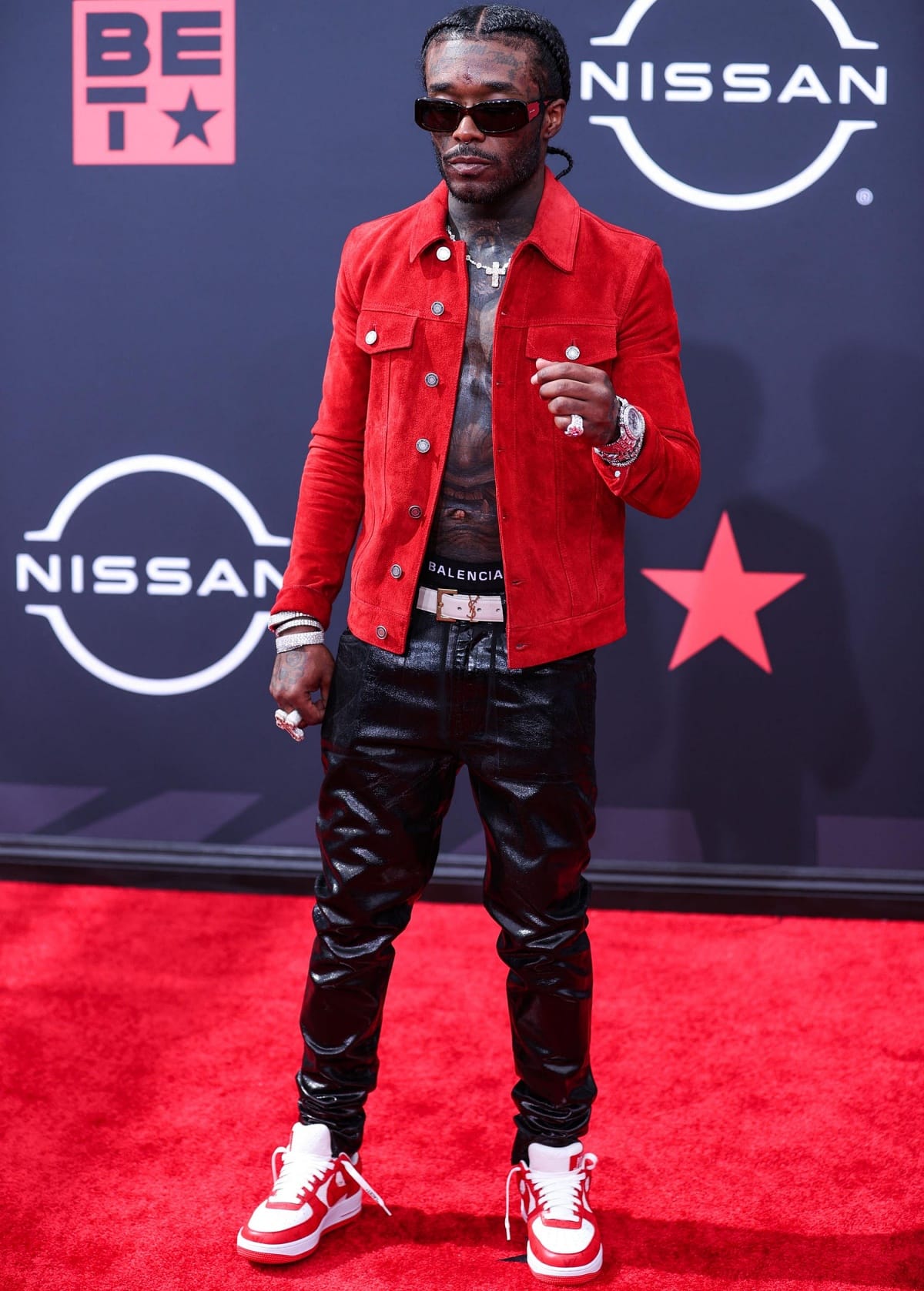 Lil Uzi Vert makes a bold statement at the 2022 BET Awards on June 26, 2022, pairing red-and-white Nike Dunks with glossy black pants, a Balenciaga belt, and a striking red suede jacket