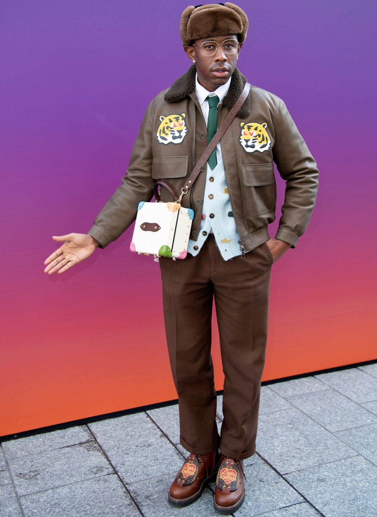 Tyler, the Creator shows off his signature eclectic style in a tiger-patched bomber jacket, fuzzy trapper hat, and playful leather boots while attending the Louis Vuitton show during Paris Fashion Week on January 20, 2022