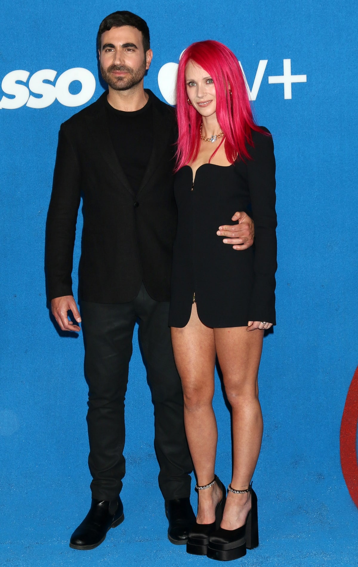 Brett Goldstein keeps it sleek in an all-black look as he poses with his Ted Lasso co-star and on-screen love interest Juno Temple, who turns heads in a daring blazer-style mini dress and sky-high platform heels that dramatically elevate her petite frame