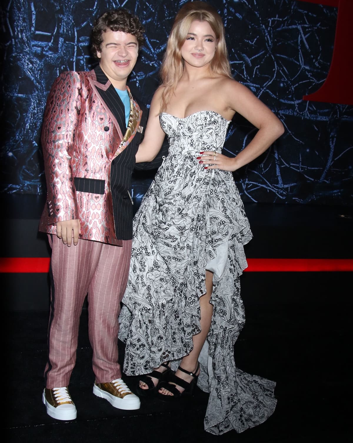 Gaten Matarazzo embraced playful suiting in a mixed-pattern Dolce Gabbana ensemble and metallic gold sneakers, while Elizabeth Yu stunned in a black-and-white ruffled high-low gown and strappy platform heels at the Stranger Things Season 4 premiere in Brooklyn on May 14, 2022