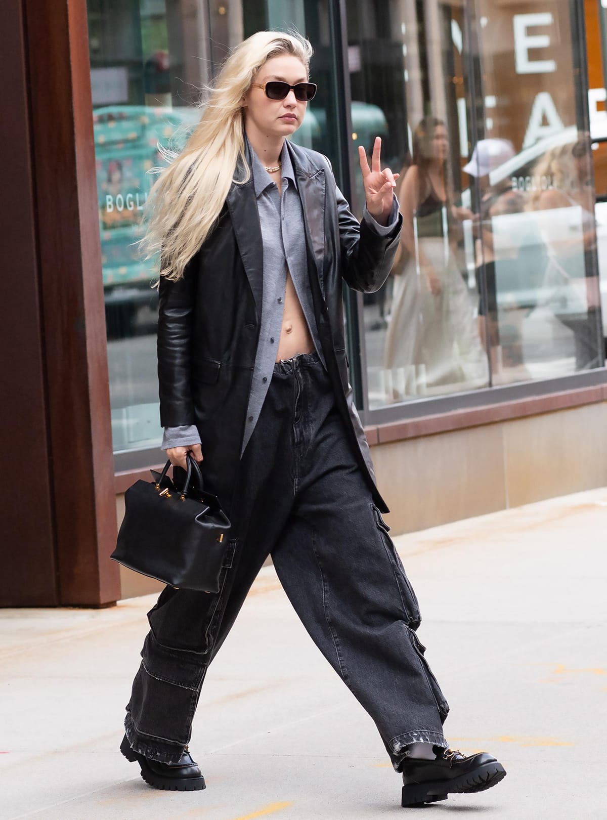 Gigi Hadid flashes her abs in a partially unbuttoned shirt teamed with Zadig Voltaire leather jacket, cargo jeans, and Gucci loafers