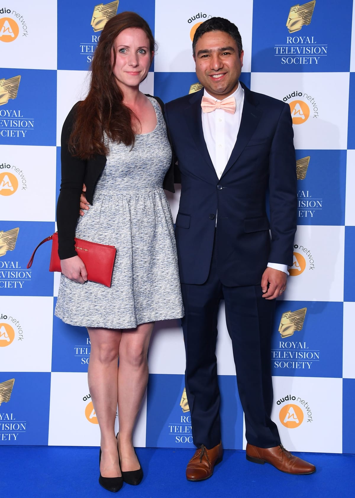 Nick Mohammed looks dapper in a navy suit and peach bow tie as he poses with his wife Becka, who stands taller in black pointed-toe heels and a textured skater dress paired with a bold red clutch at the Royal Television Society Programme Awards
