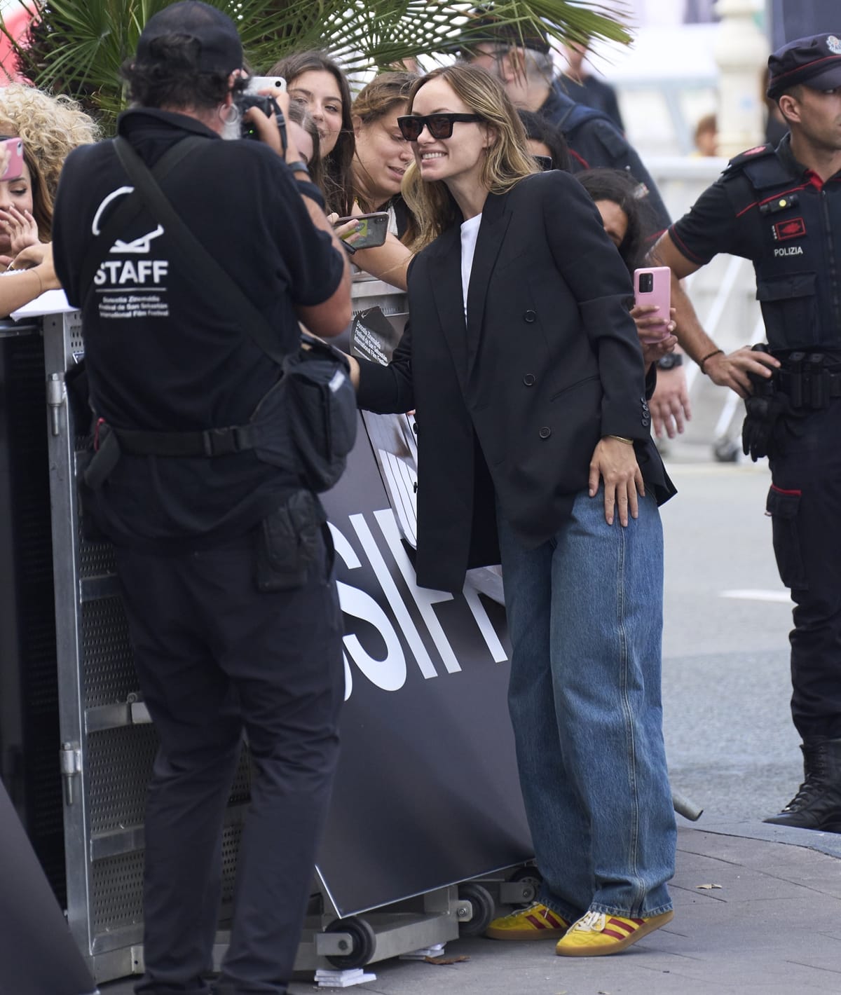 Effortlessly chic: Olivia Wilde connects with fans, showcasing her yellow Adidas x Gucci Gazelle sneakers, baggy jeans, and a sharp tuxedo jacket