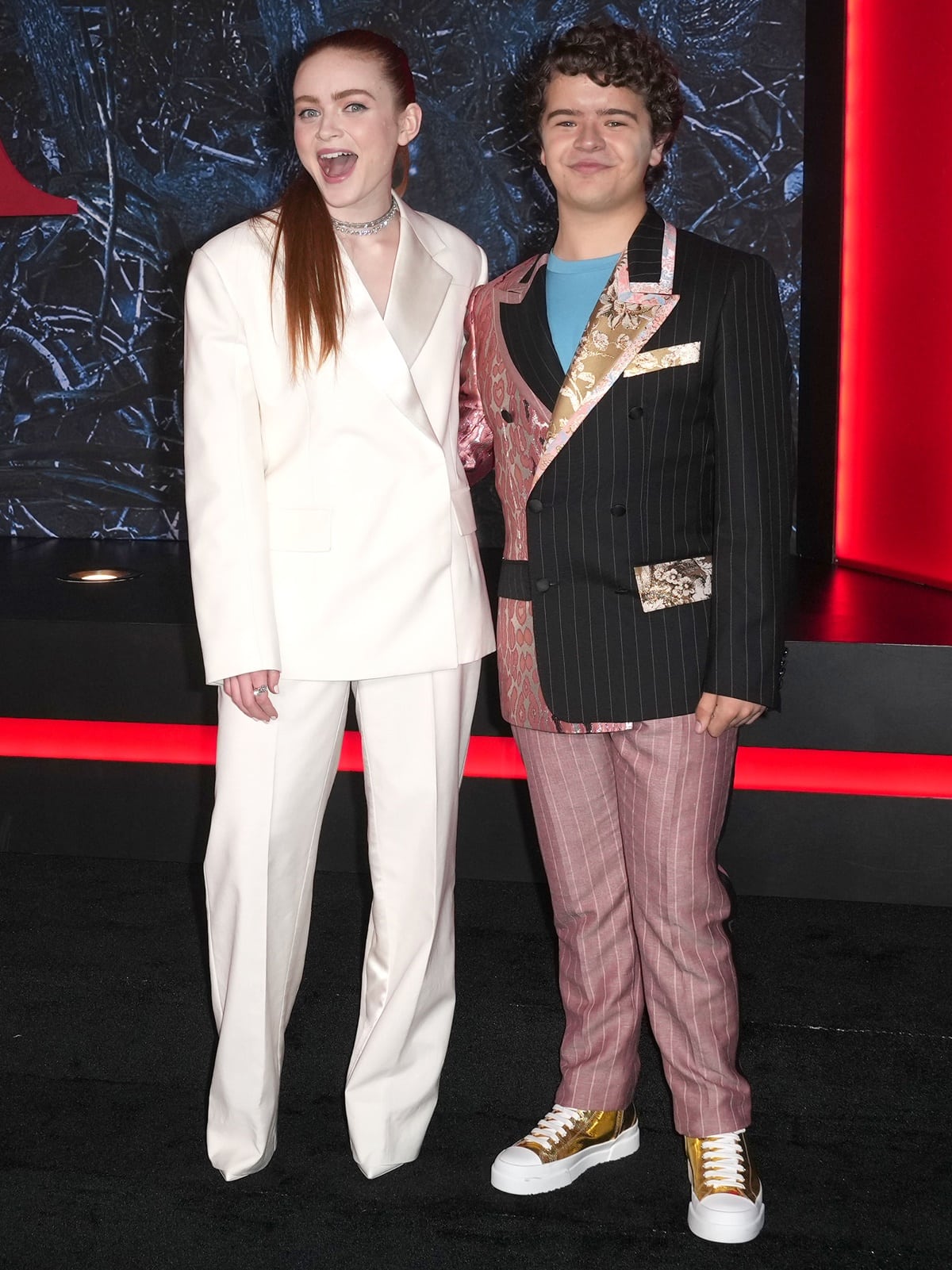 Sadie Sink looked effortlessly chic in a crisp white Prada suit paired with subtle heels, while Gaten Matarazzo made a bold statement in a custom mixed-pattern Dolce Gabbana suit and eye-catching metallic gold platform sneakers at the Stranger Things Season 4 premiere in Brooklyn