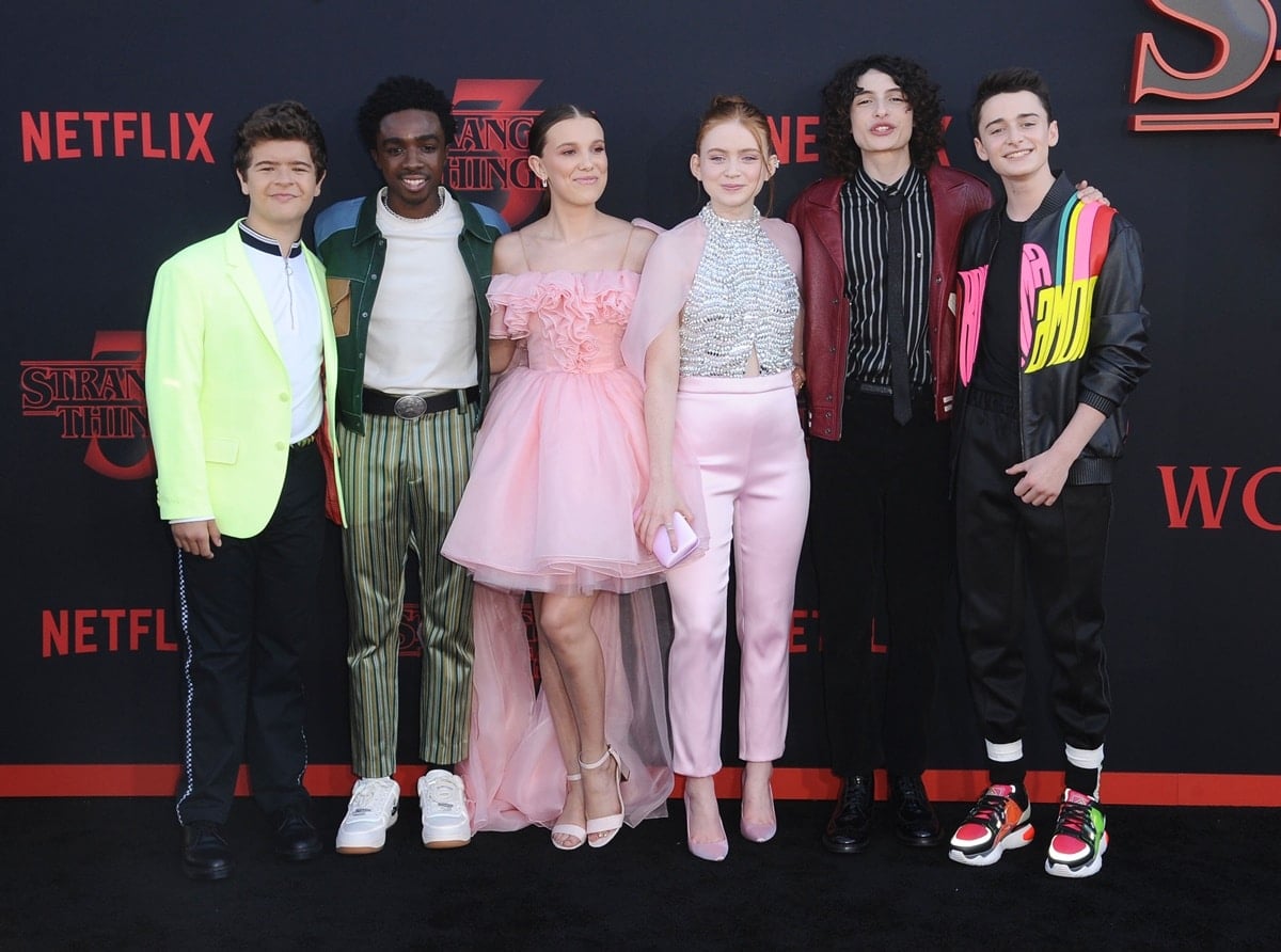 The Stranger Things cast lit up the black carpet at the Season 3 premiere, with Millie Bobby Brown in a pink ruffled Rodarte dress and ankle-strap heels, Sadie Sink in sparkly separates and satin pumps, and the boys adding flair with sneakers, loafers, and bold jackets