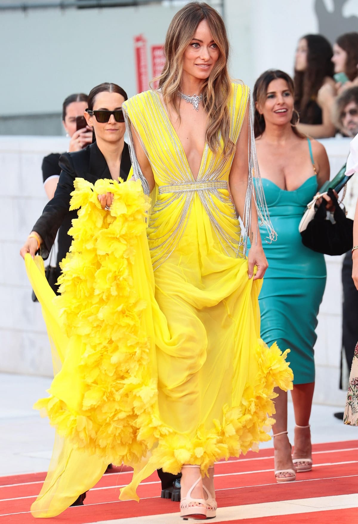 Olivia Wilde turned heads in a custom yellow Gucci gown adorned with crystal fringe, pairing the look with barely visible strappy nude heels that subtly elongated her frame