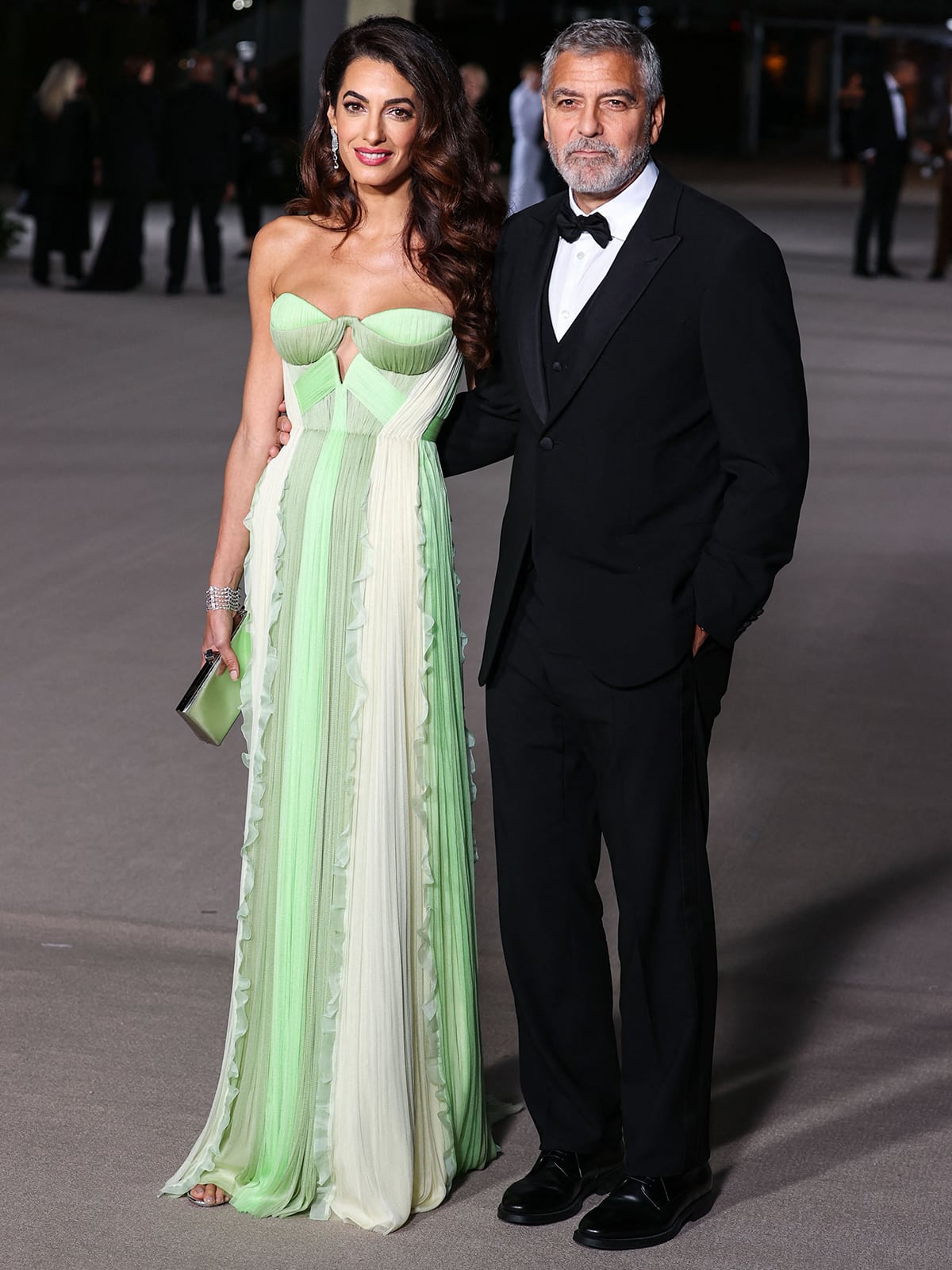 Amal Clooney commands the red carpet in a flowing Del Core green gown, pairing ethereal movement with sleek evening sandals as George Clooney keeps things classic at her side