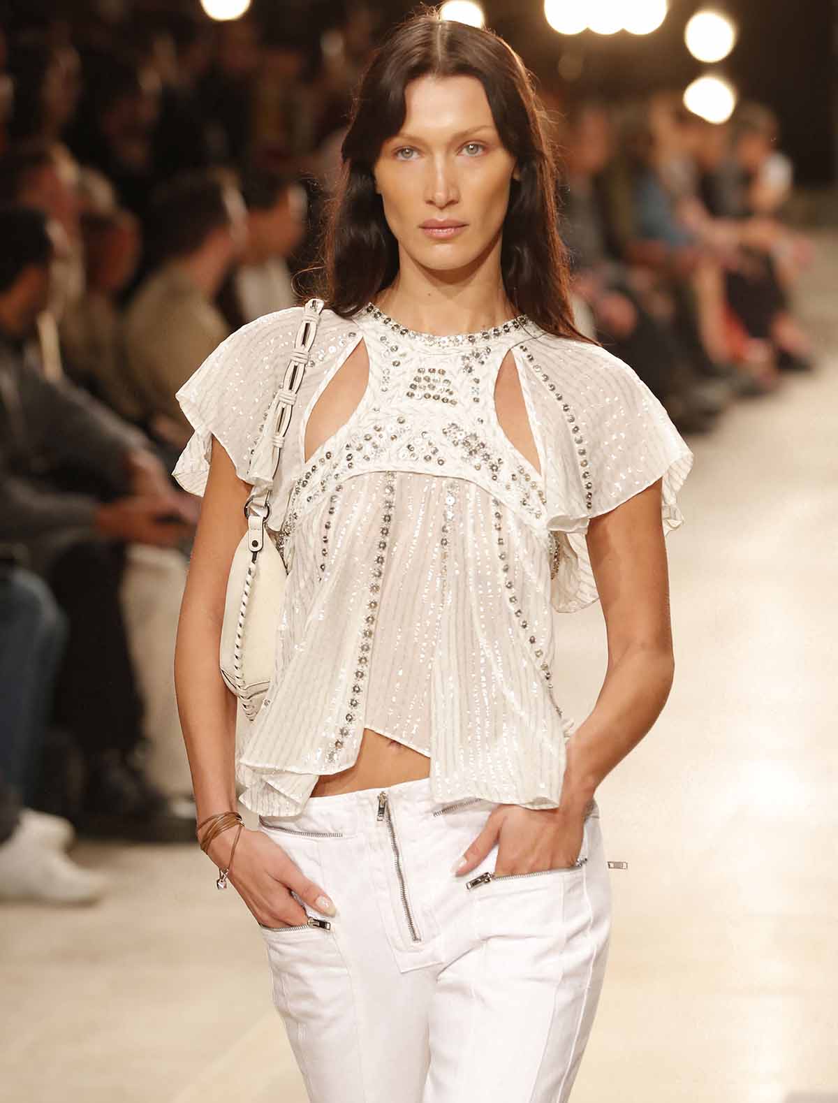 Bella Hadid wears a wavy brunette hairstyle and neutral makeup with nude pink lipstick