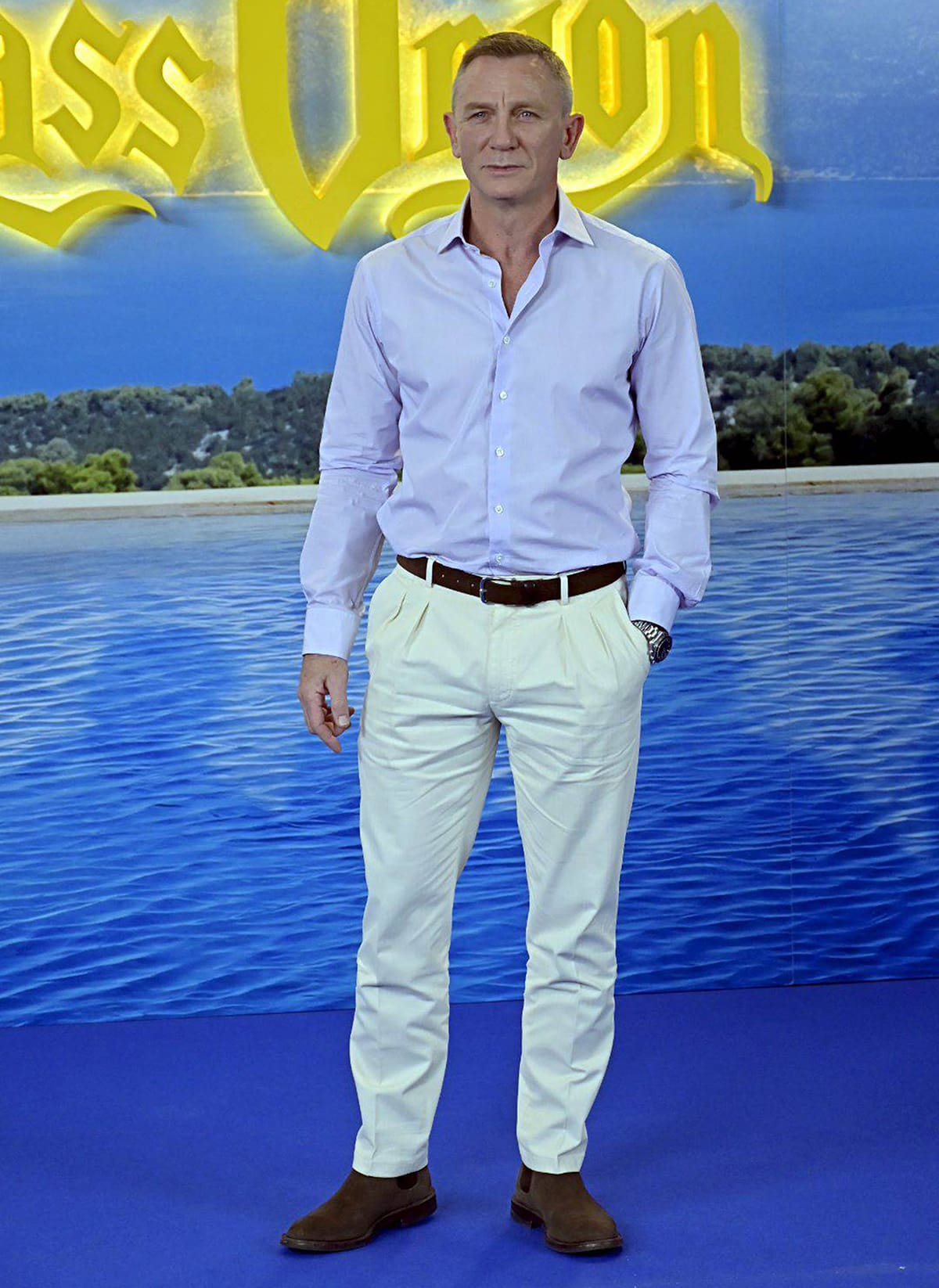 Daniel Craig keeps it effortlessly polished at the Glass Onion photocall, pairing a pale lavender shirt with cream trousers, a brown belt, and matching suede Chelsea boots for a refined smart-casual look