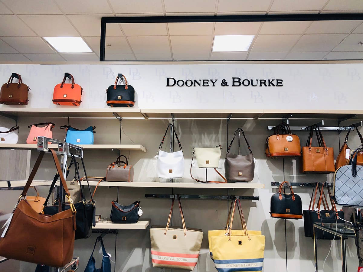 A Dooney Bourke boutique display showcases the brand’s heritage craftsmanship—once proudly made in Norwalk, Connecticut, where the company is still based—though most bags today are produced in China, with select collections made in Italy, Costa Rica, and Mexico