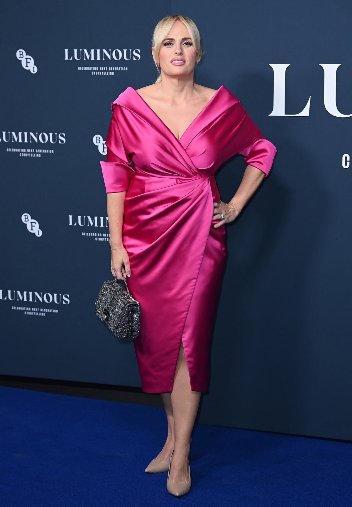 Rebel Wilson keeps it sleek and streamlined in a hot pink Rhea Costa wrap midi dress, finishing the look with nude pointed-toe pumps that subtly lengthen her silhouette at the BFI London Film Festival Luminous Gala on September 29, 2022