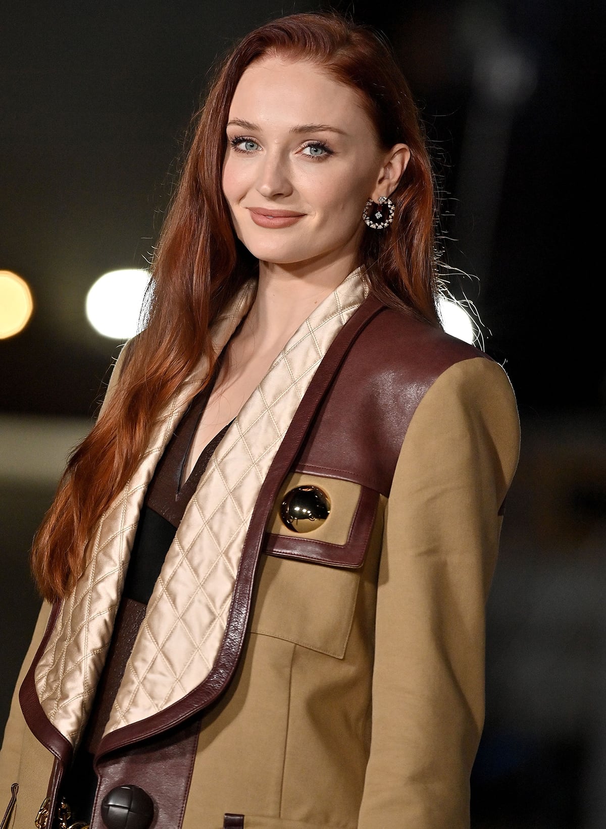 Sophie Turner wears her long red tresses in side-parted waves and coordinates her matte brown lipstick with her outfit