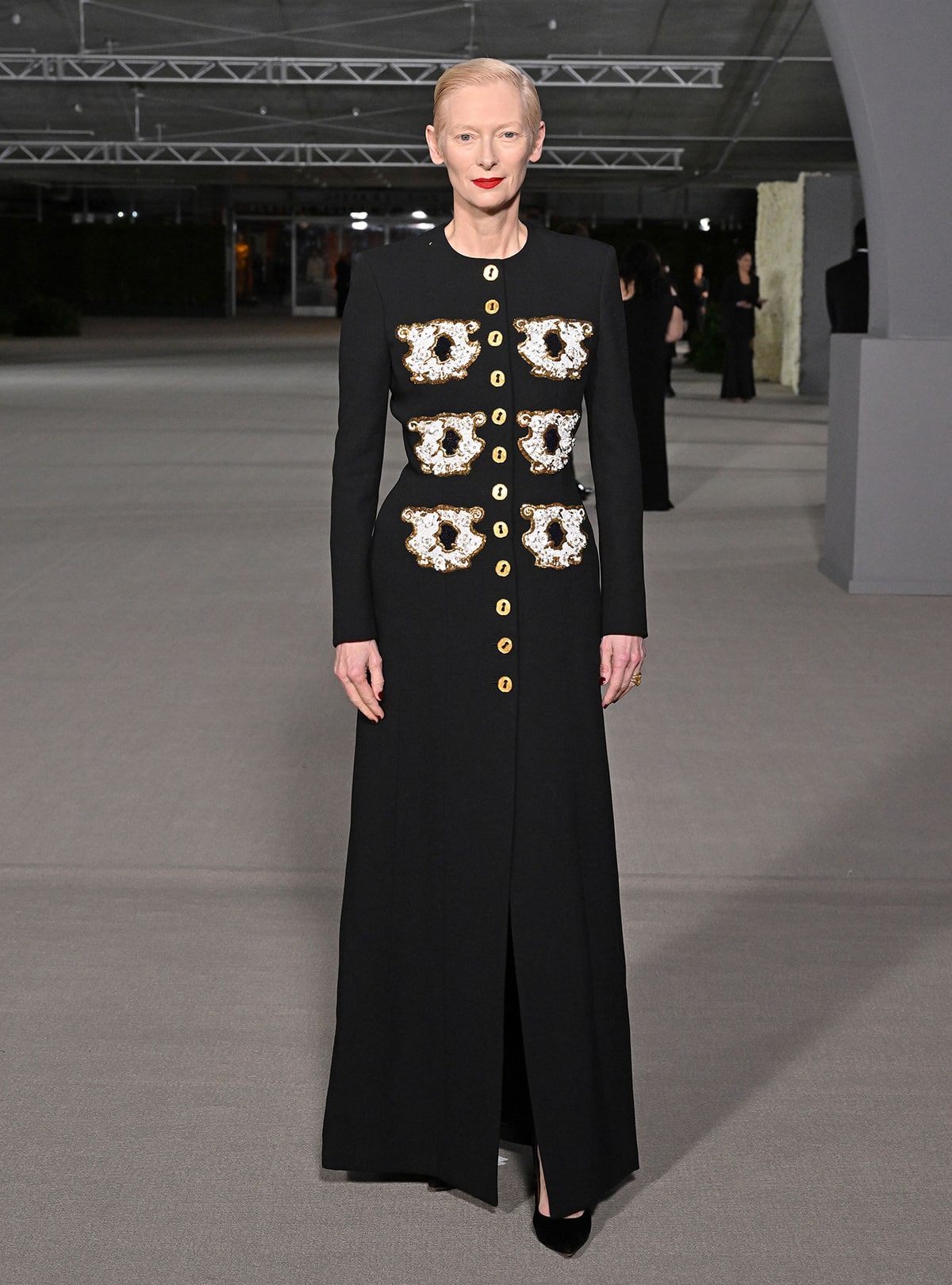 Tilda Swinton embodies refined couture in a Schiaparelli dress coat, defined by surreal teacup embroidery and polished gold buttons that elevate the minimalist silhouette