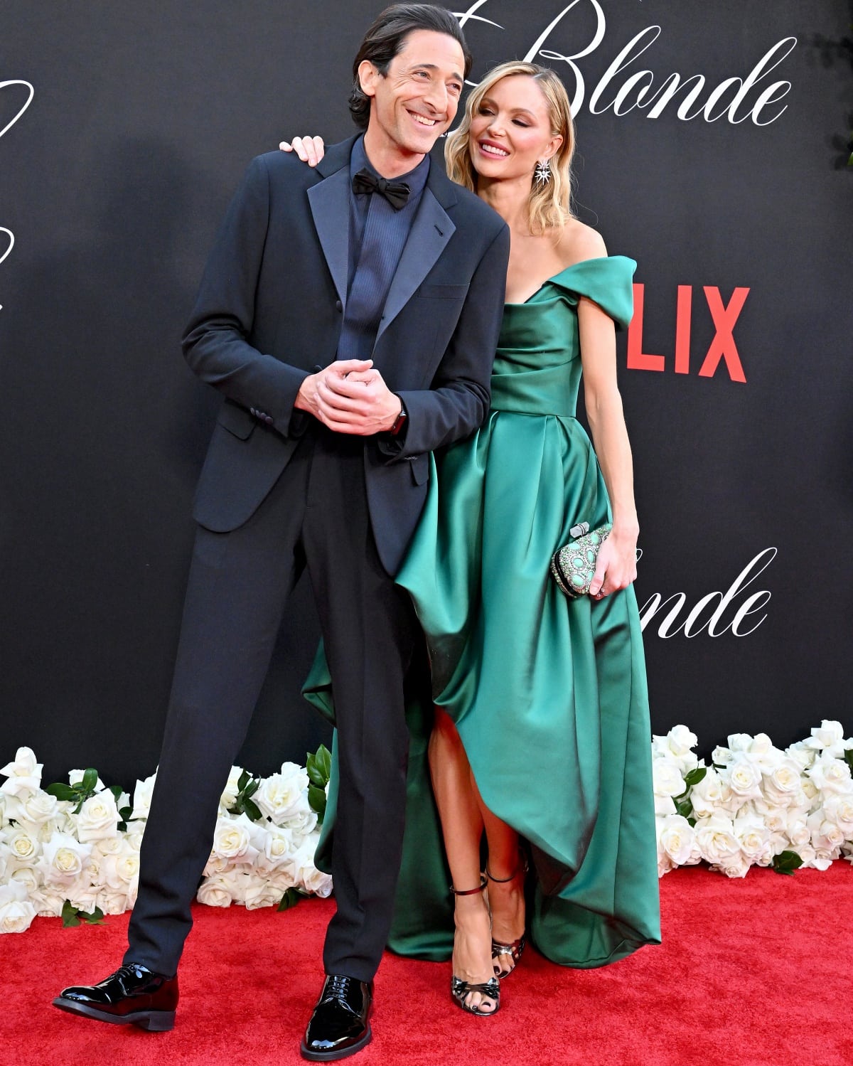 Adrien Brody and Georgina Chapman share a joyful moment at the Los Angeles premiere of Blonde on September 14, 2022, with Chapman glowing in a satin emerald green off-the-shoulder gown paired with embellished black ankle-strap heels and a sparkling clutch
